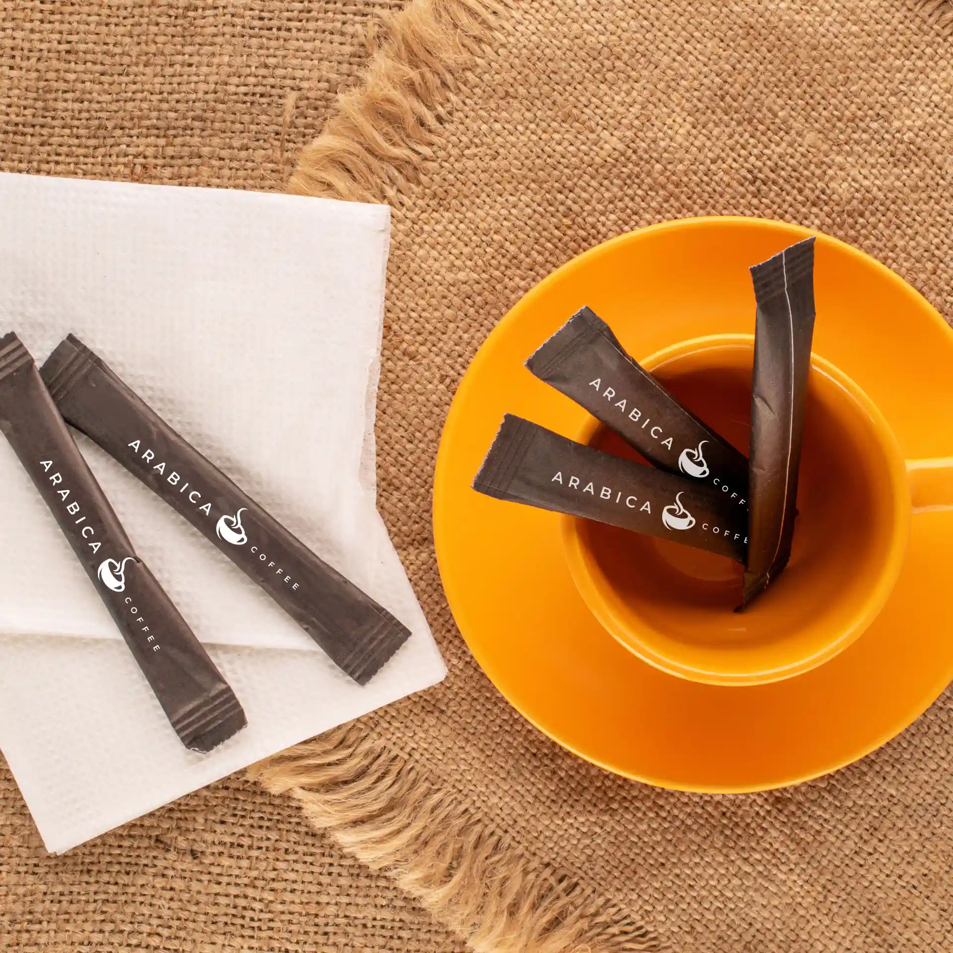 Image de bâtonnets de sucre brun avec logo placés sur une serviette blanche à côté d'une tasse orange sur une surface texturée.