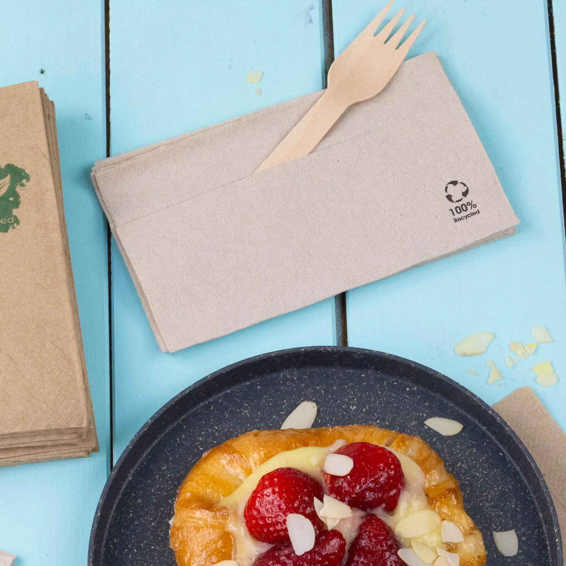 Serviettes en papier recyclé, montrant une fourchette en bois, sur une surface en bois bleu clair.