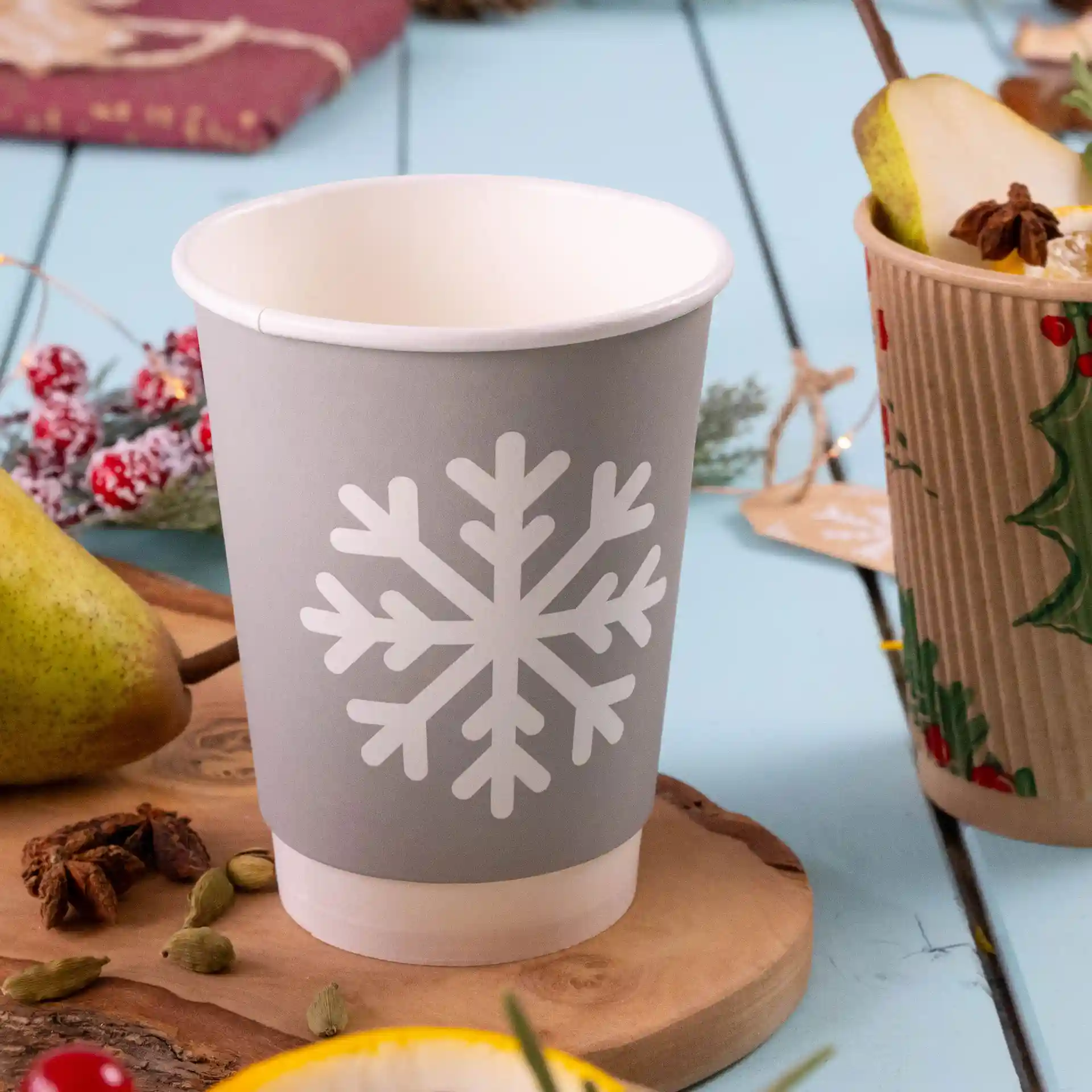 Bicchiere di carta grigio a doppia parete con design di fiocchi di neve bianchi, capacità di 12 oz, su una superficie di legno con oggetti decorativi.