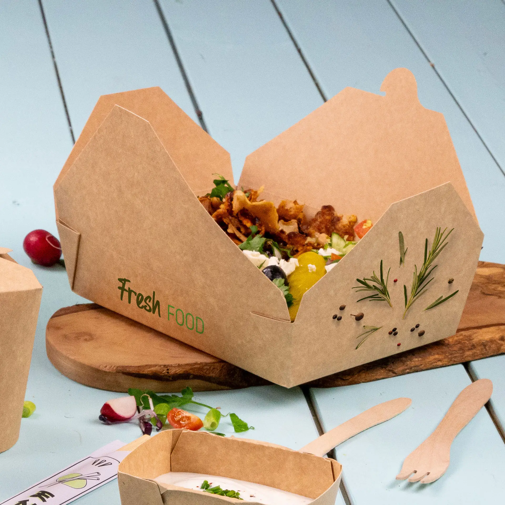 Eine Takeaway-Box mit kartonartiger Textur und "Frische Lebensmittel" Druck, gefüllt mit einem Salat und garniert, auf einem Holzbrett.
