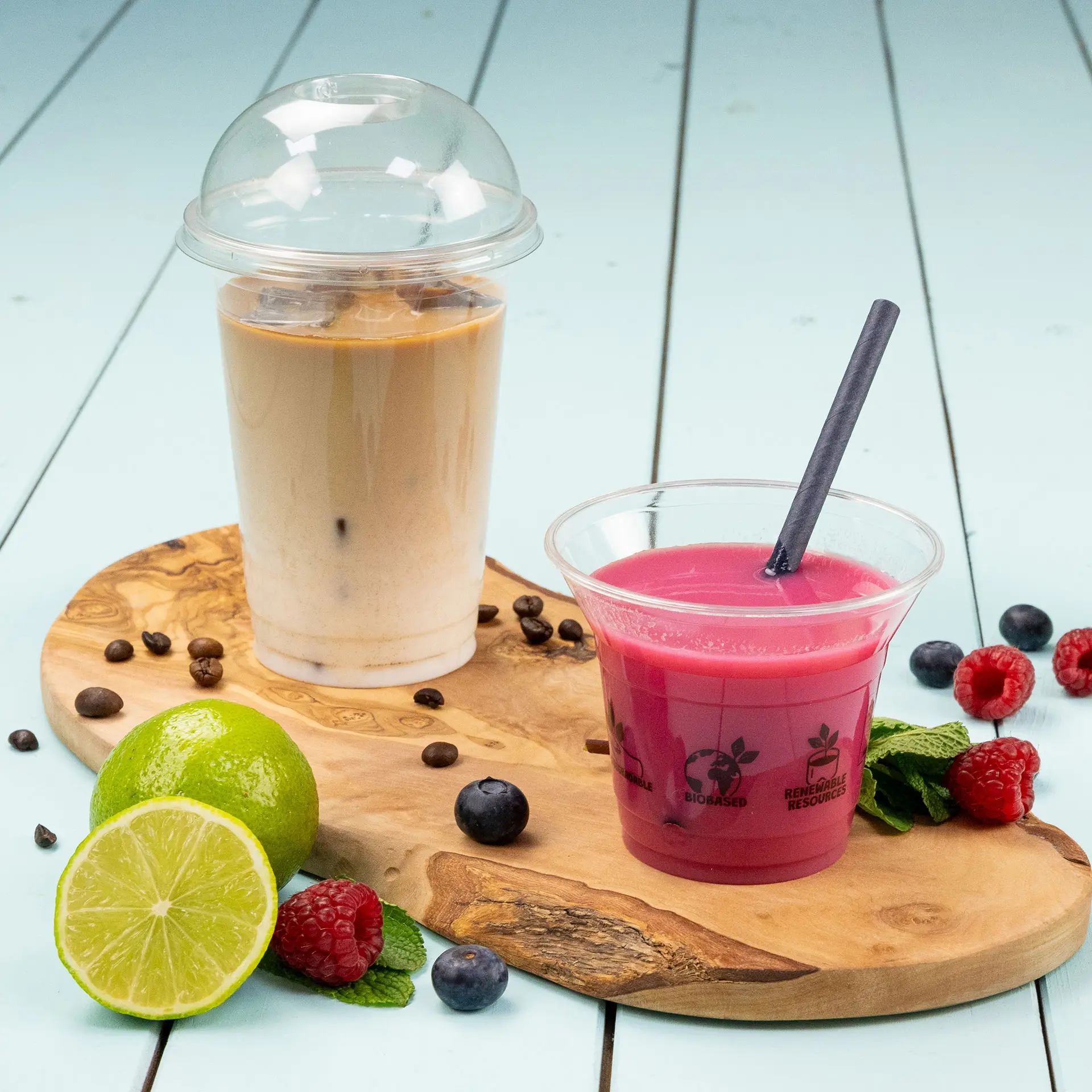 Des verres transparents remplis de boissons froides, y compris du café glacé et une boisson rose, sur une planche en bois.
