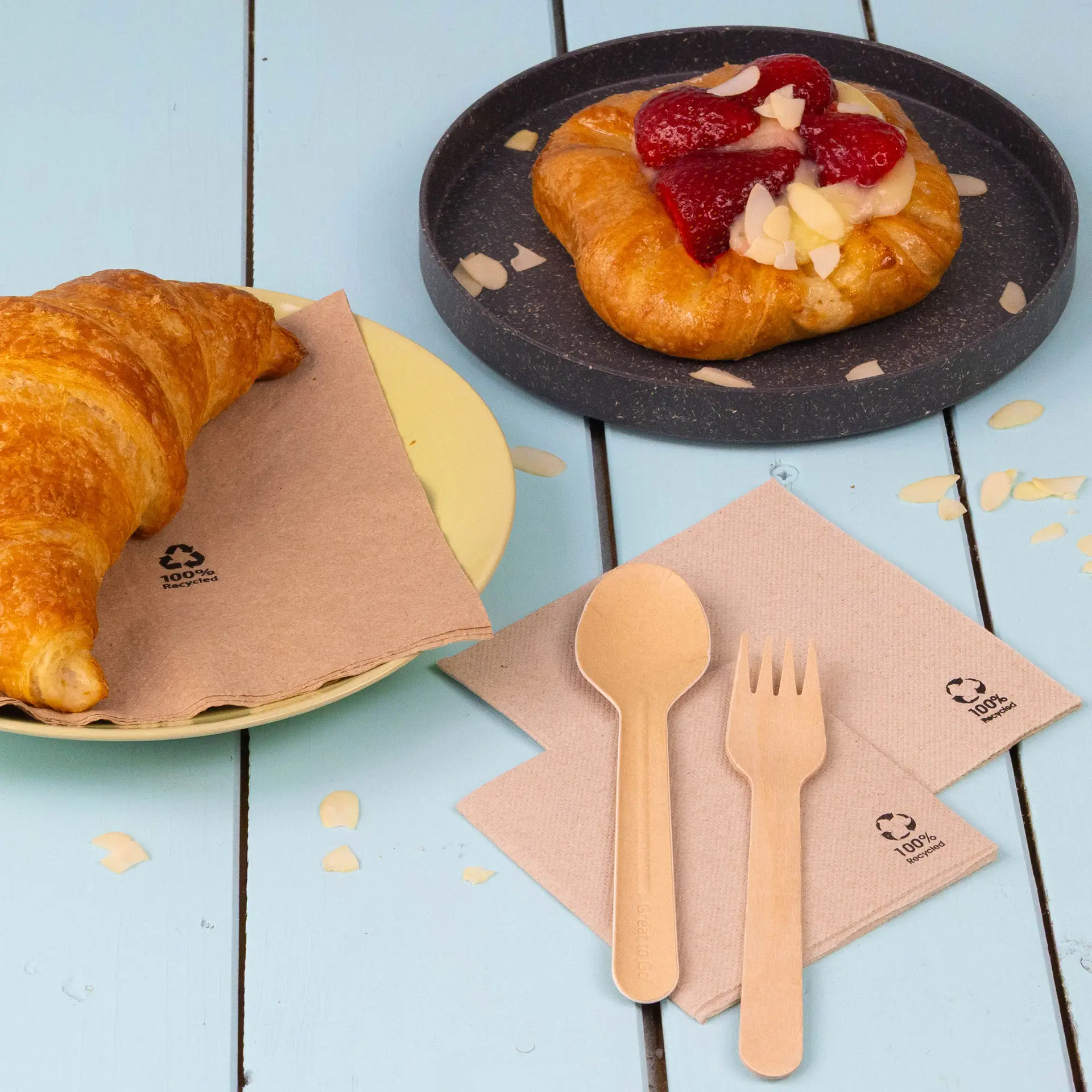 Une tasse sur une assiette blanche avec un biscuit, entourée d'une tasse de framboises et de granola, et de serviettes en papier.