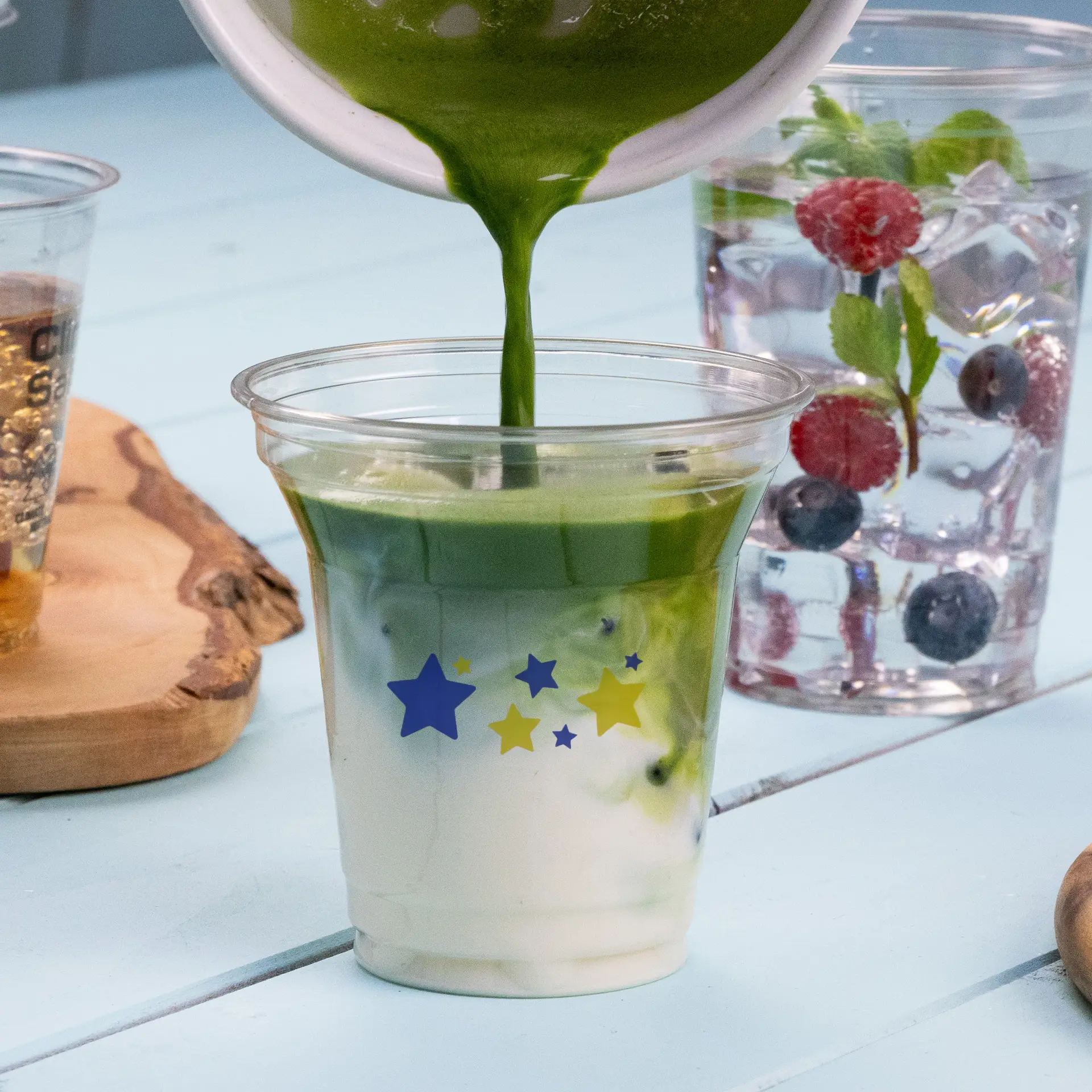 Versare una bevanda verde in un bicchiere trasparente rPET da 8 oz con design a stelle; altre bevande in secondo piano.