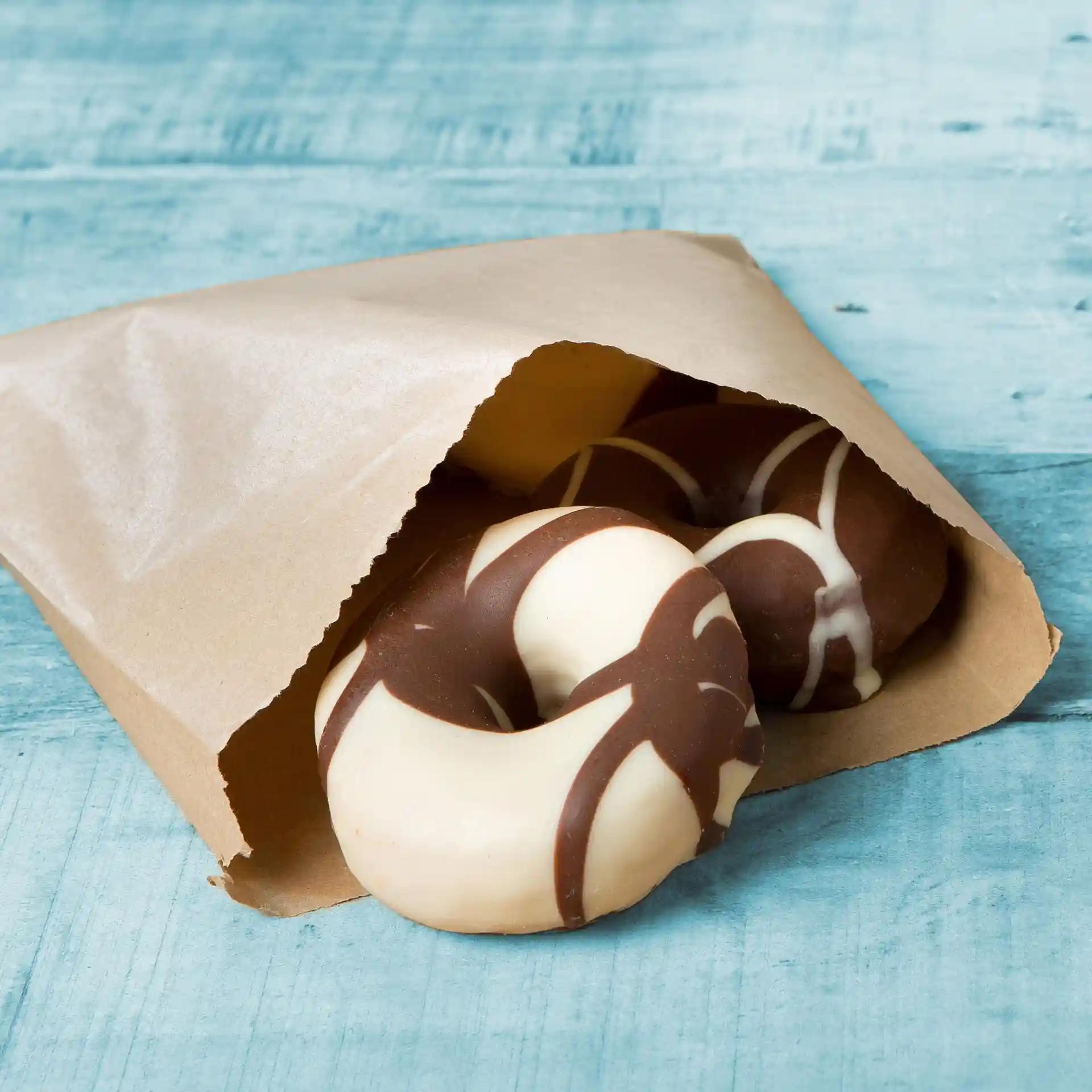 Busta di carta marrone parzialmente aperta, che rivela due ciambelle ricoperte di cioccolato all'interno.