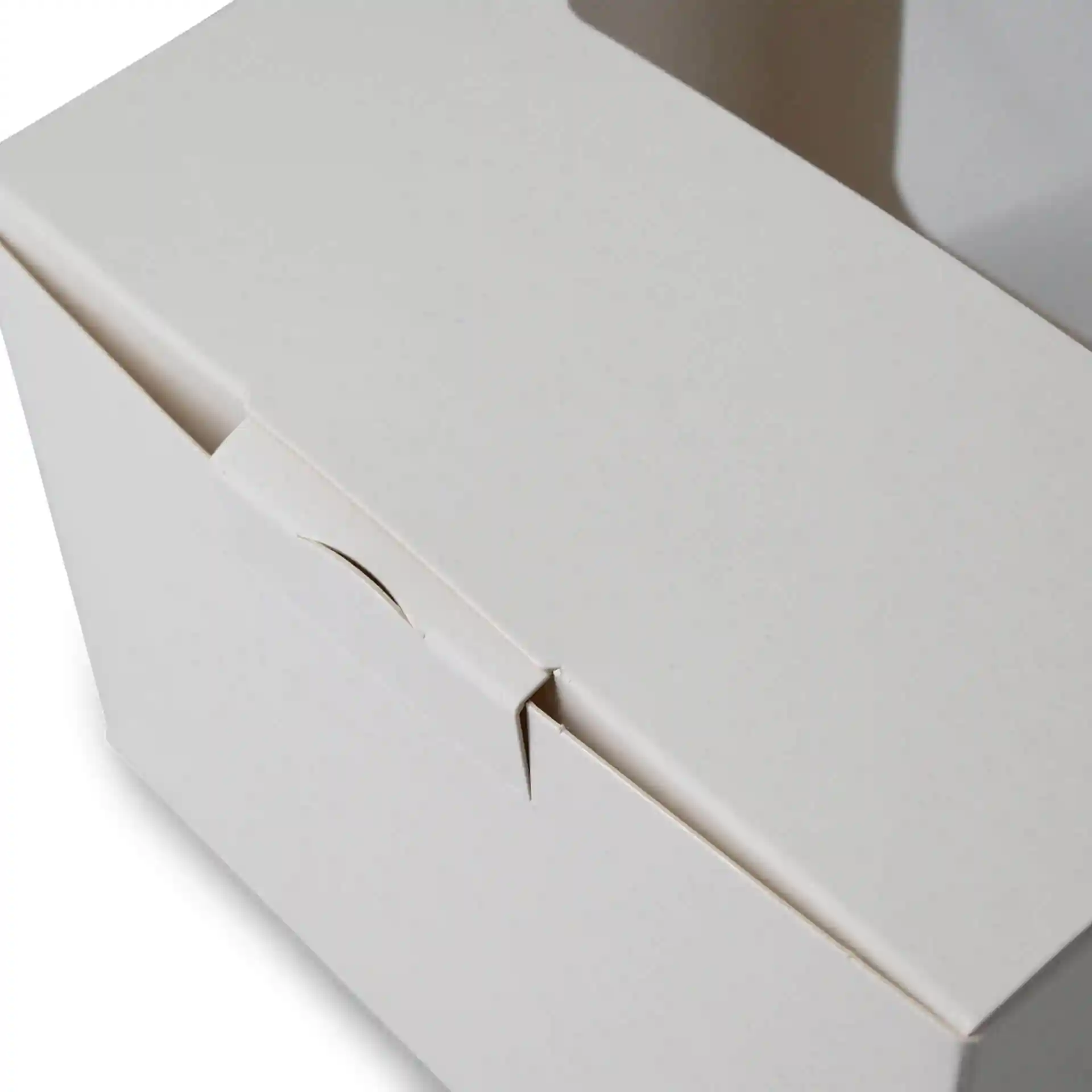 Boîte à pâtisserie blanche avec une fenêtre en cellulose, montrant la fermeture supérieure et une partie du côté. Dimensions : 13 x 11 x 8 cm.