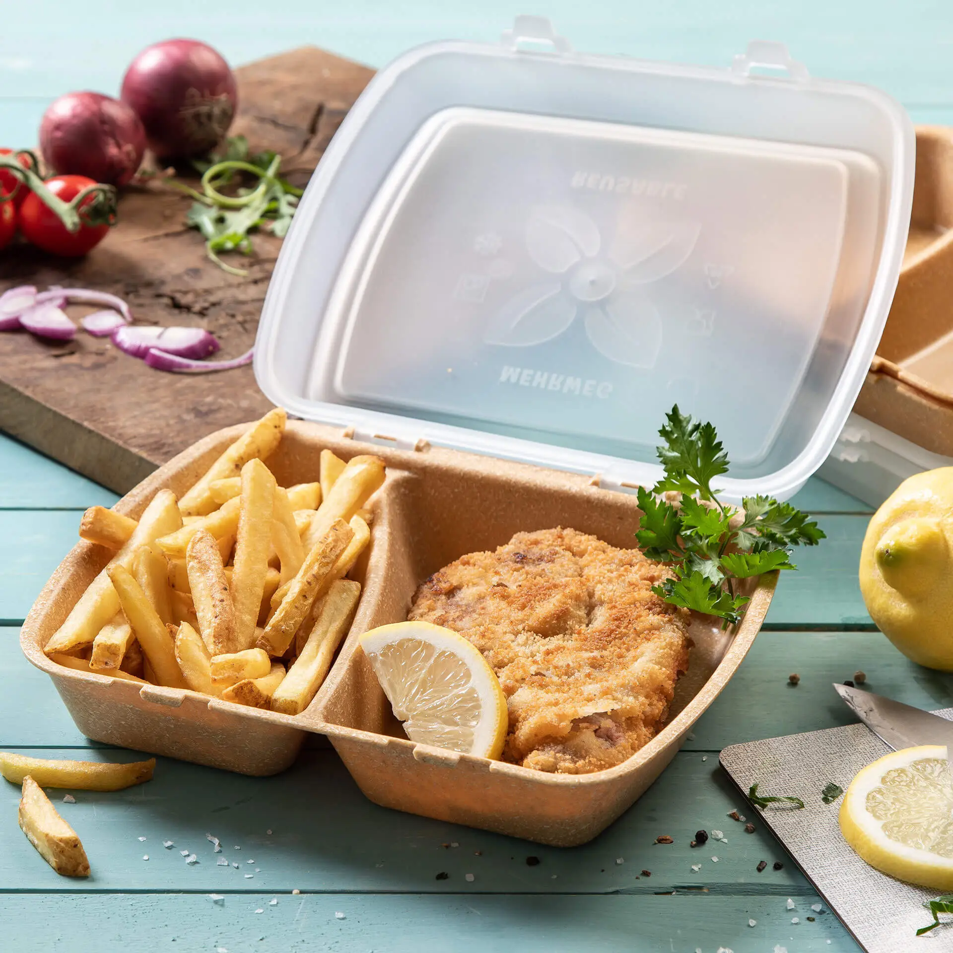 Conteneur avec poulet frit, frites et tranche de citron, dans une boîte en plastique transparente sur une surface bleue.