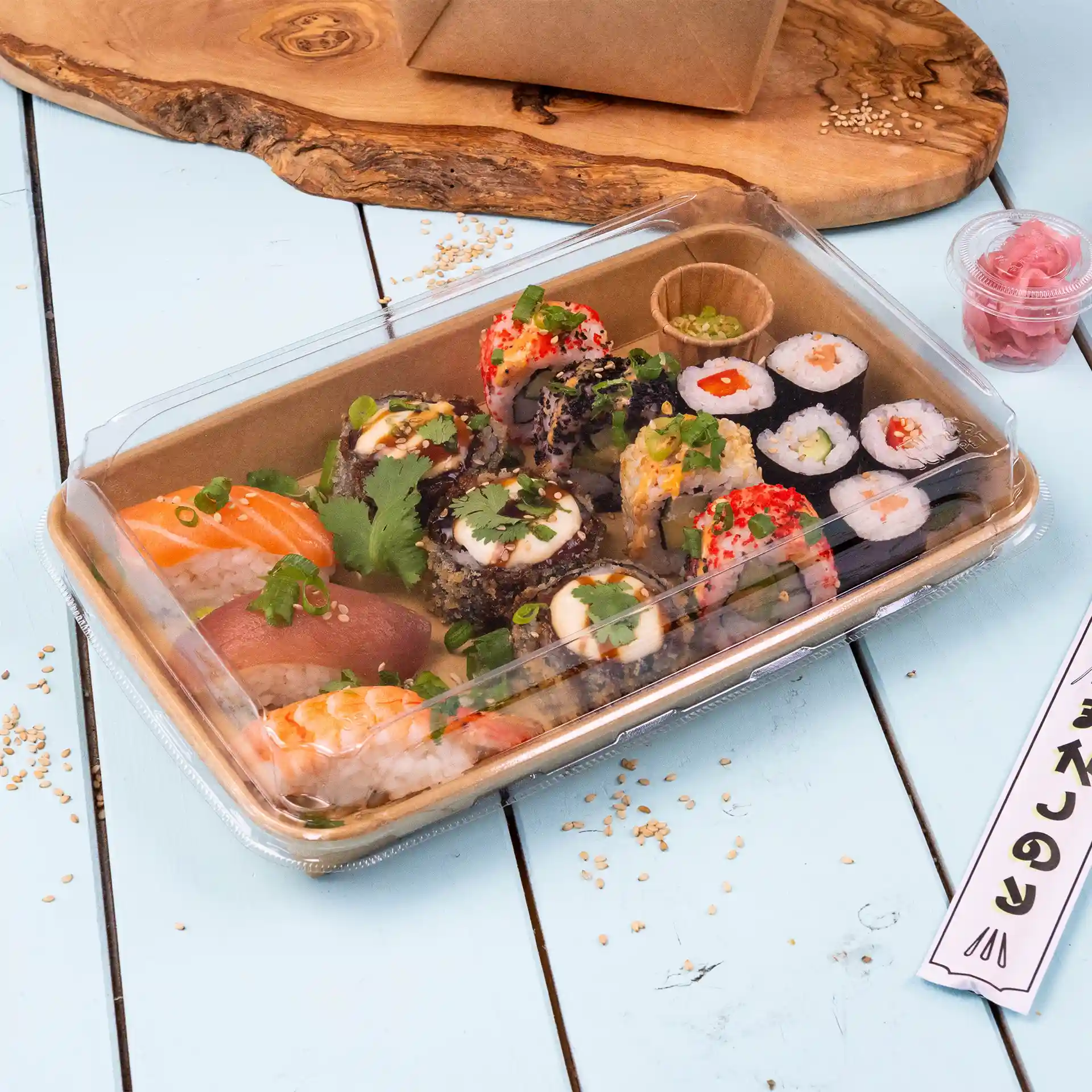 Transparente Sushi-Box-Deckel mit verschiedenen Sushi-Rollen, darunter Lachs und Thunfisch, garniert mit Kräutern und serviert mit eingelegtem Ingwer.