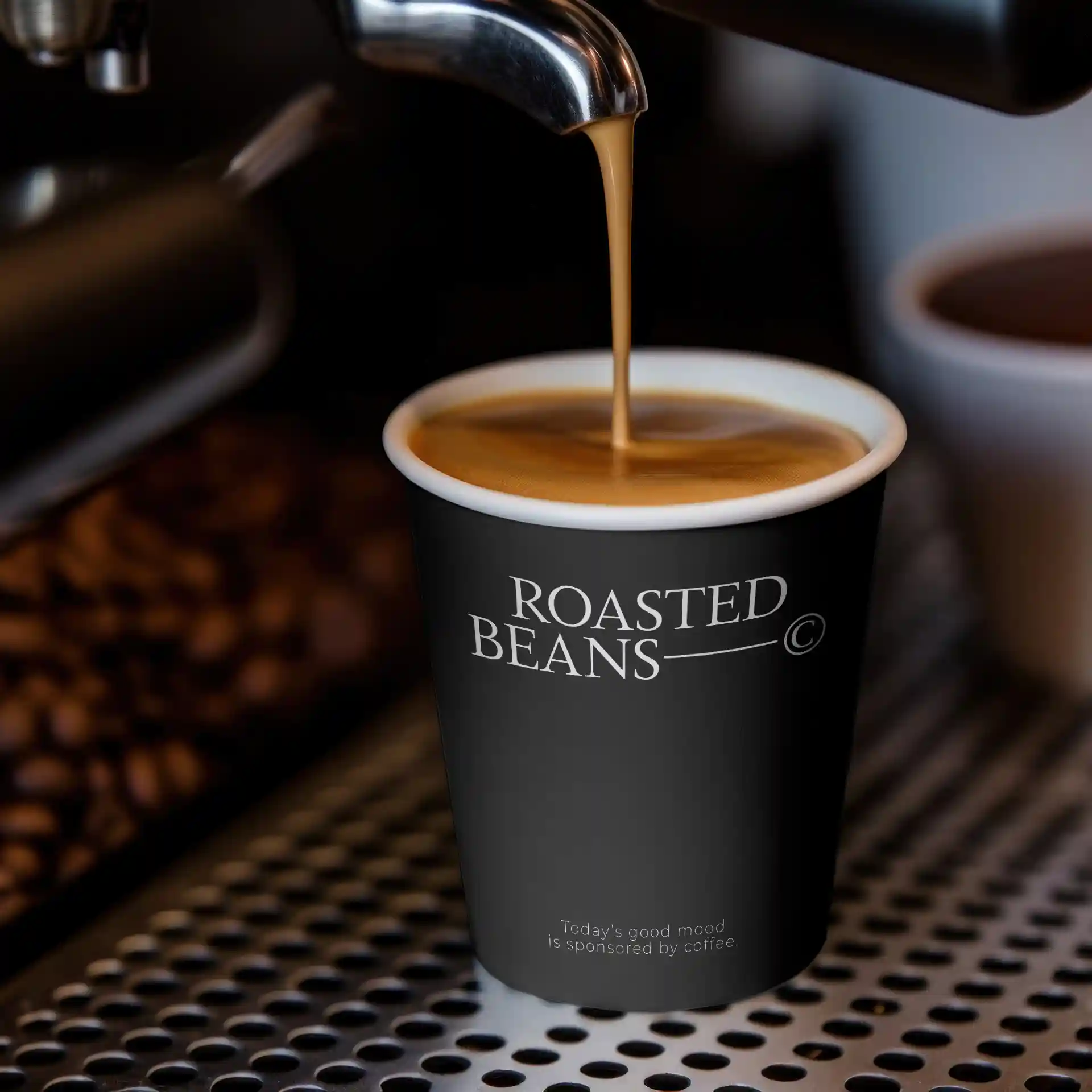 Schwarzer Becher mit Logo, gefüllt mit Kaffee, auf einer metallischen Oberfläche mit Kaffeebohnen im Hintergrund.