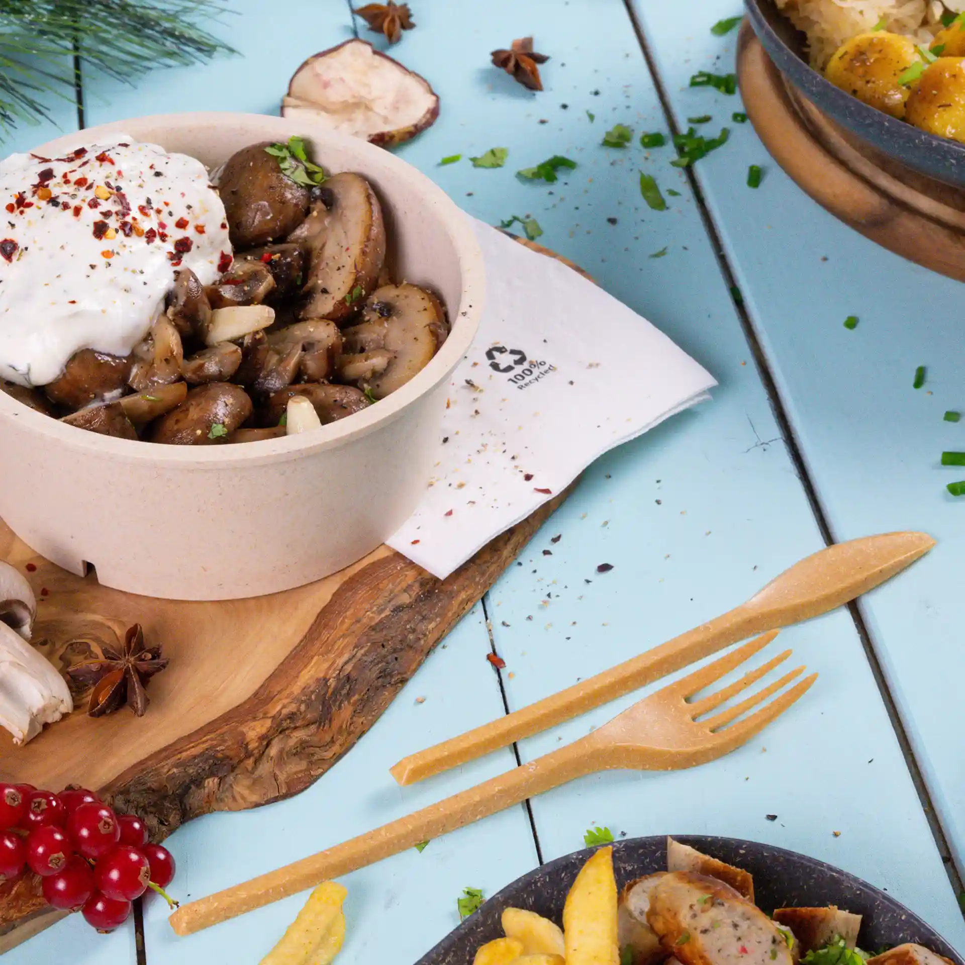 Bol de champignons sautés surmonté de yaourt et d'épices, accompagné d'une fourchette et d'un couteau en bois sur une surface bleue.