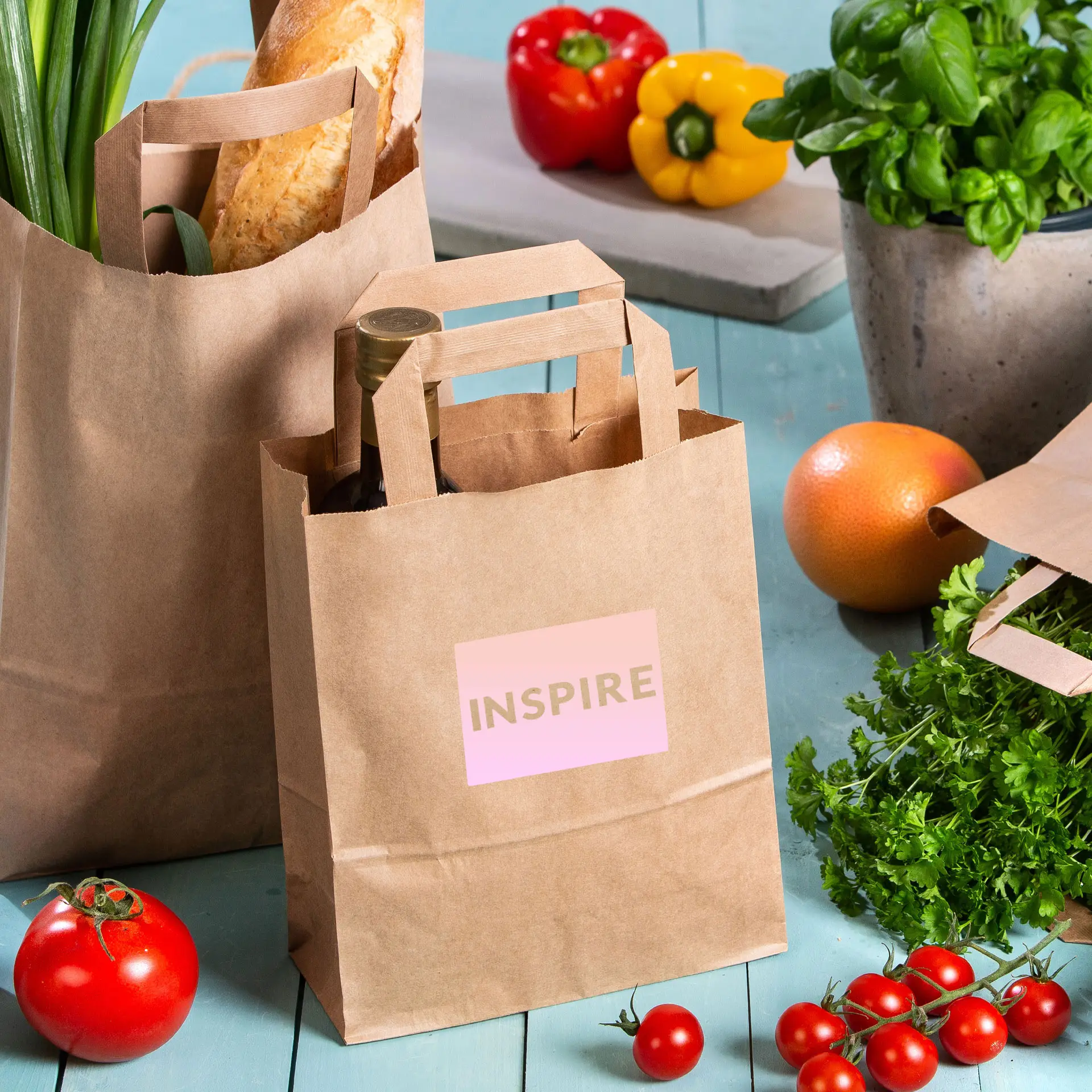 Sacs en papier kraft marron avec une étiquette imprimée "INSPIRE", entourés de légumes frais et d'herbes.