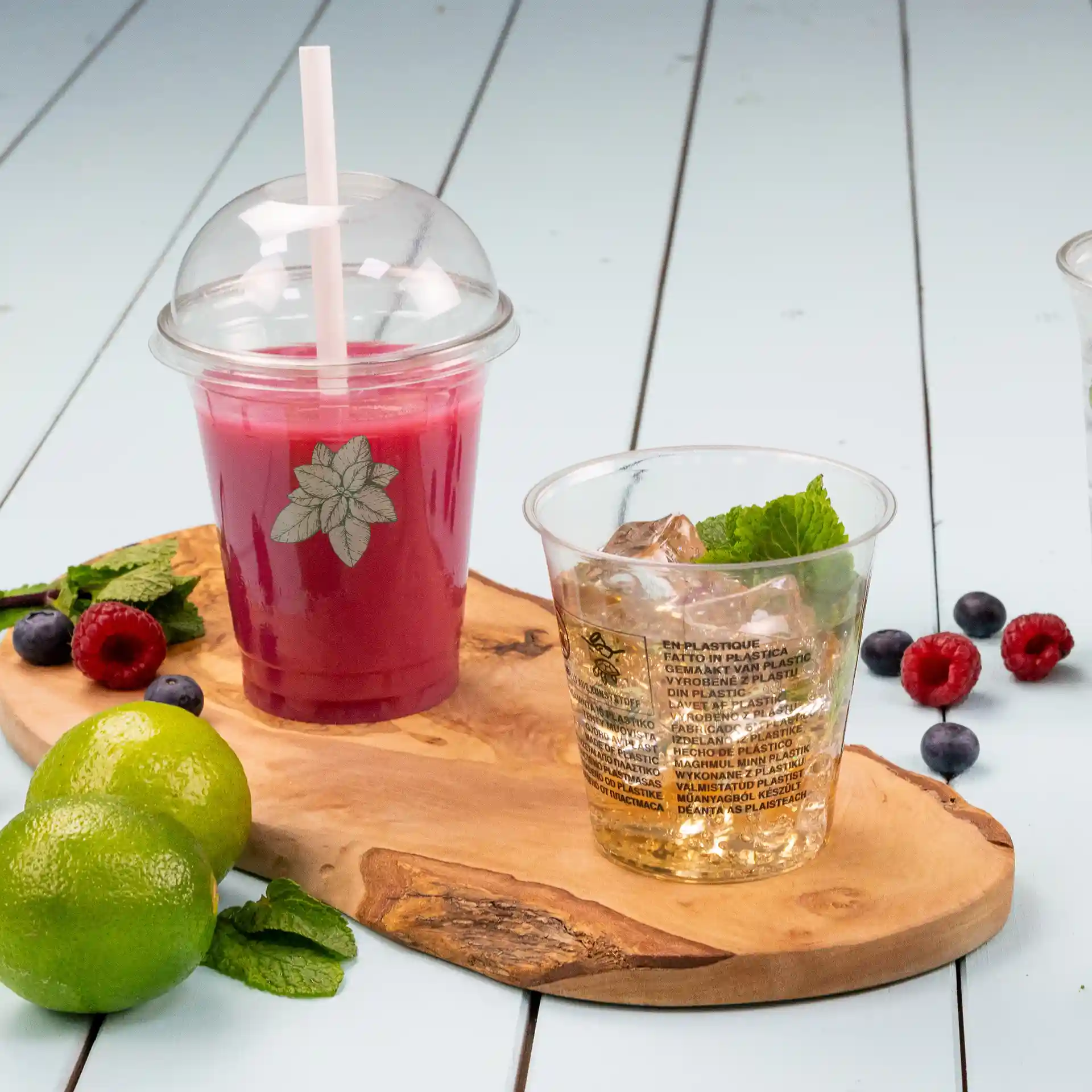 Bicchiere rPET trasparente da 12 oz con coperchio a cupola e cannuccia, riempito con una bevanda rossa, accanto a un bicchiere di ghiaccio e menta.