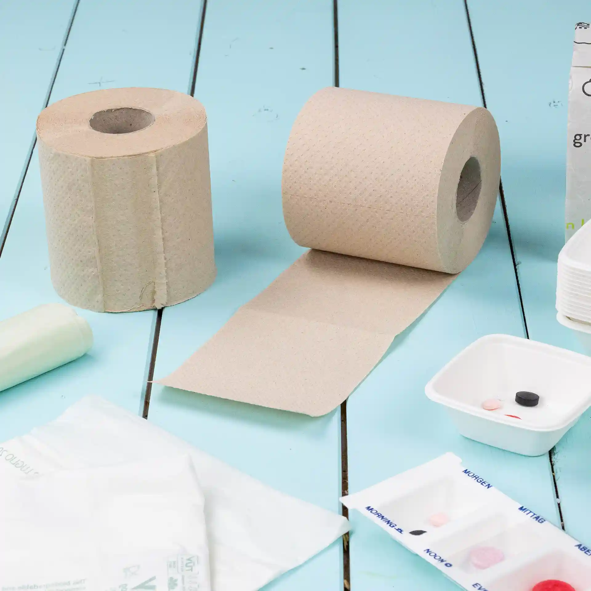 Deux rouleaux de papier toilette brun en papier recyclé, 2 plis, avec un rouleau partiellement déroulé sur une surface bleue.