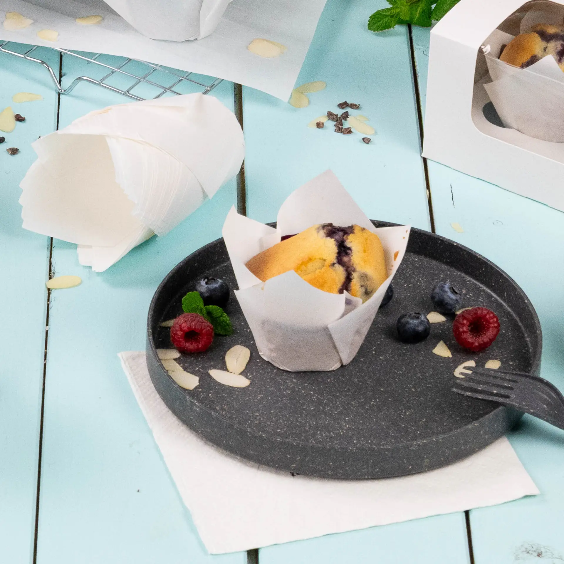 Un moule à muffin blanc avec du papier anti-graisse sur une assiette noire ; garni de framboises, myrtilles et tranches d'amande.