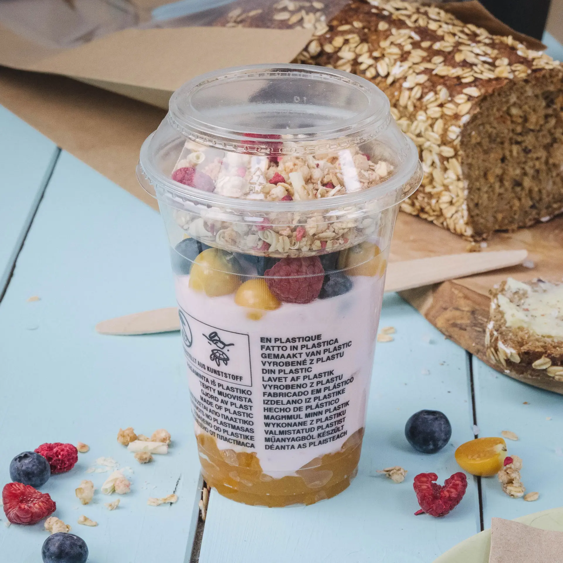 Conteneur avec yaourt, fruits et granola dans un gobelet en PET transparent, accompagné d'une tranche de pain à l'avoine.
