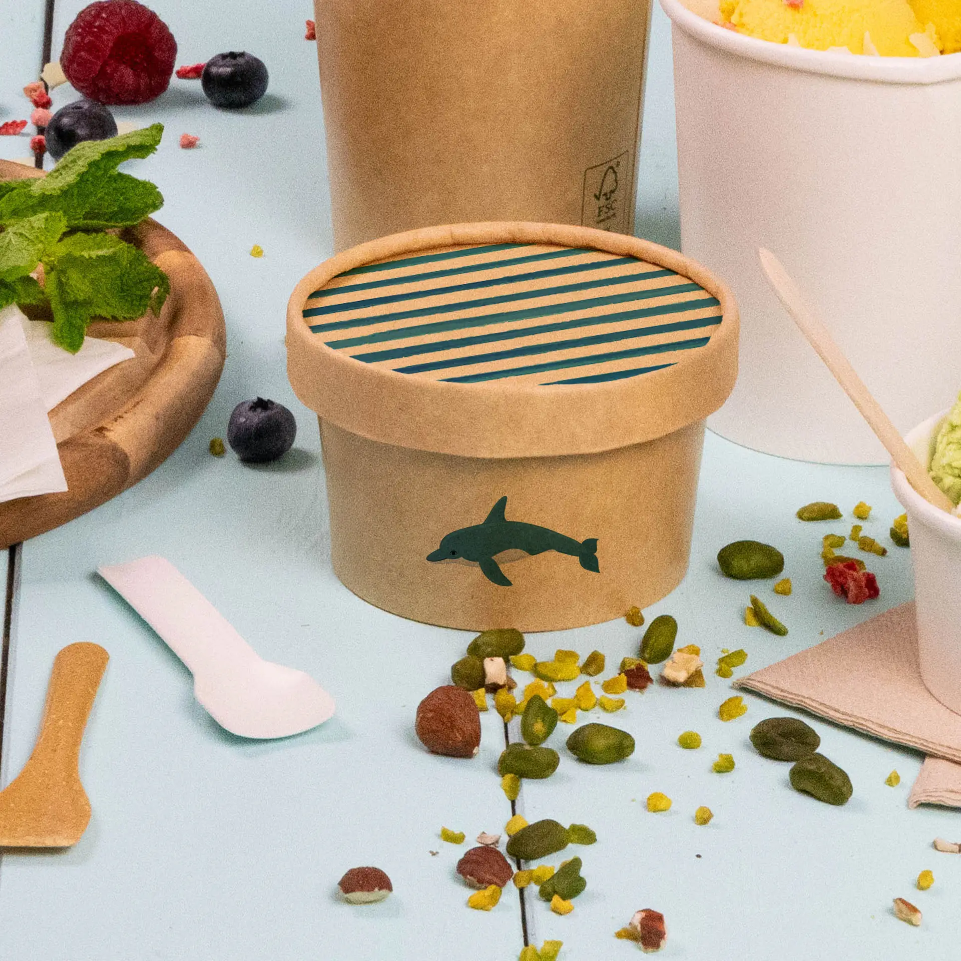 Un couvercle en carton brun pour des pots de crème glacée, avec un design de dauphin et un intérieur rayé bleu, avec des aliments à proximité.