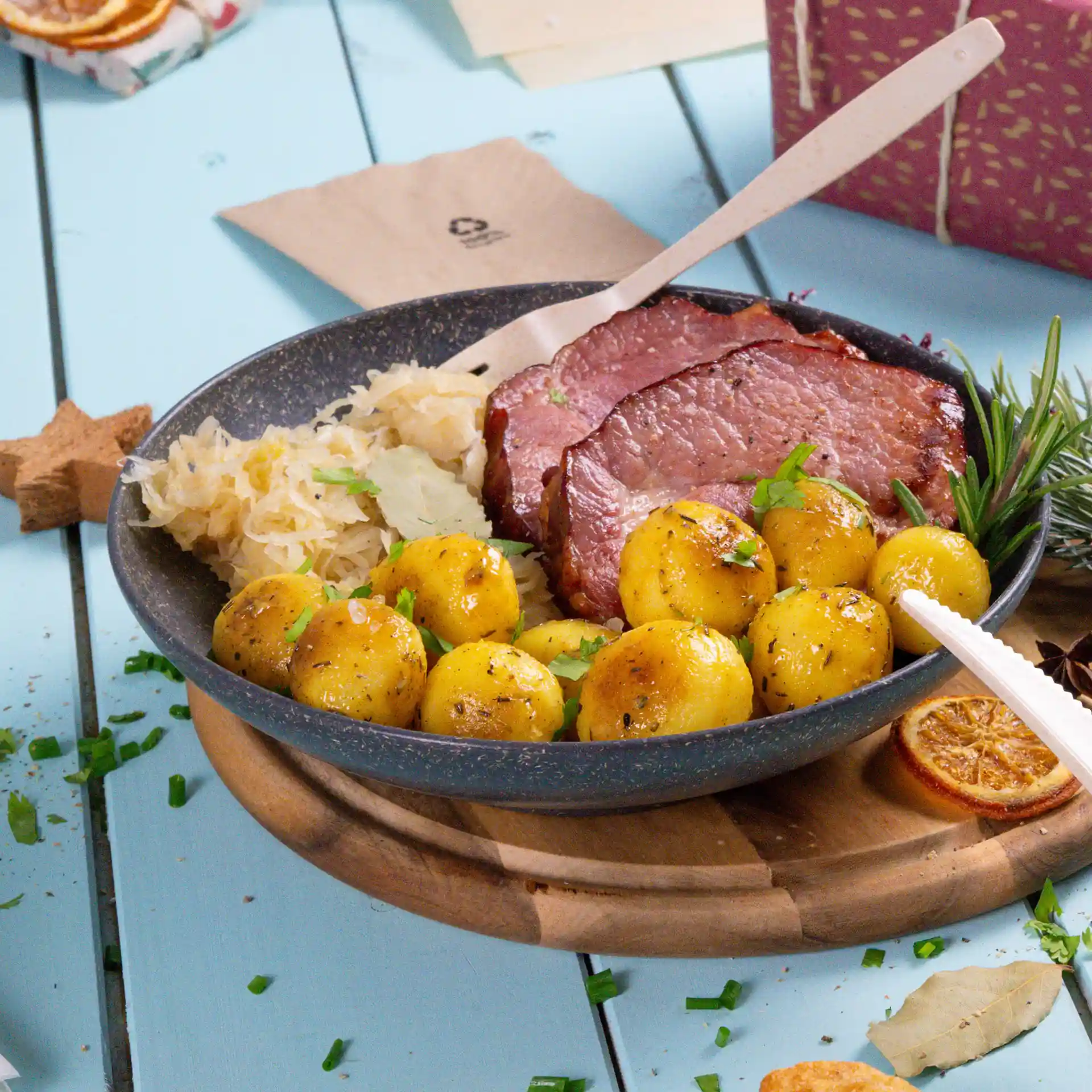 Tiefe runde graue Schale mit geschnittenem Fleisch, gekochten Kartoffeln und Sauerkraut, auf einem Holzbrett.