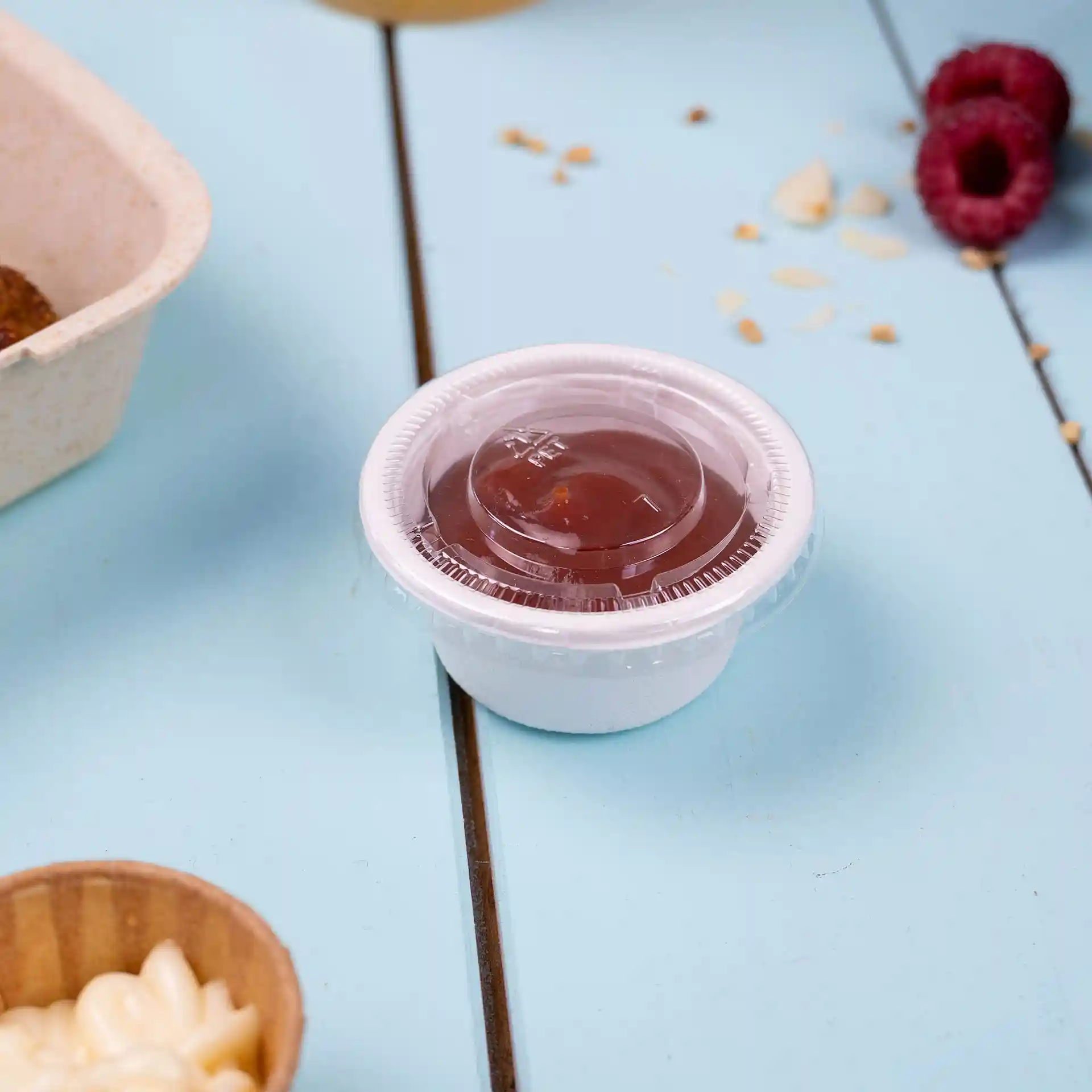 Conteneur rond transparent avec un couvercle transparent, contenant une sauce rouge, placé sur une surface bleue.