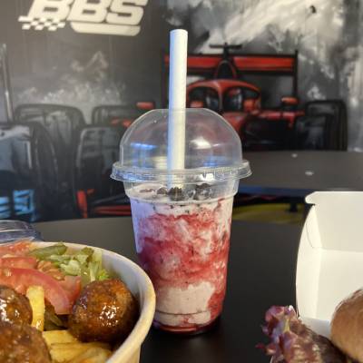 Milkshake dans un gobelet transparent avec une paille, entouré d'un bol de salade, de frites et de boulettes de viande sur une table à thème de course.