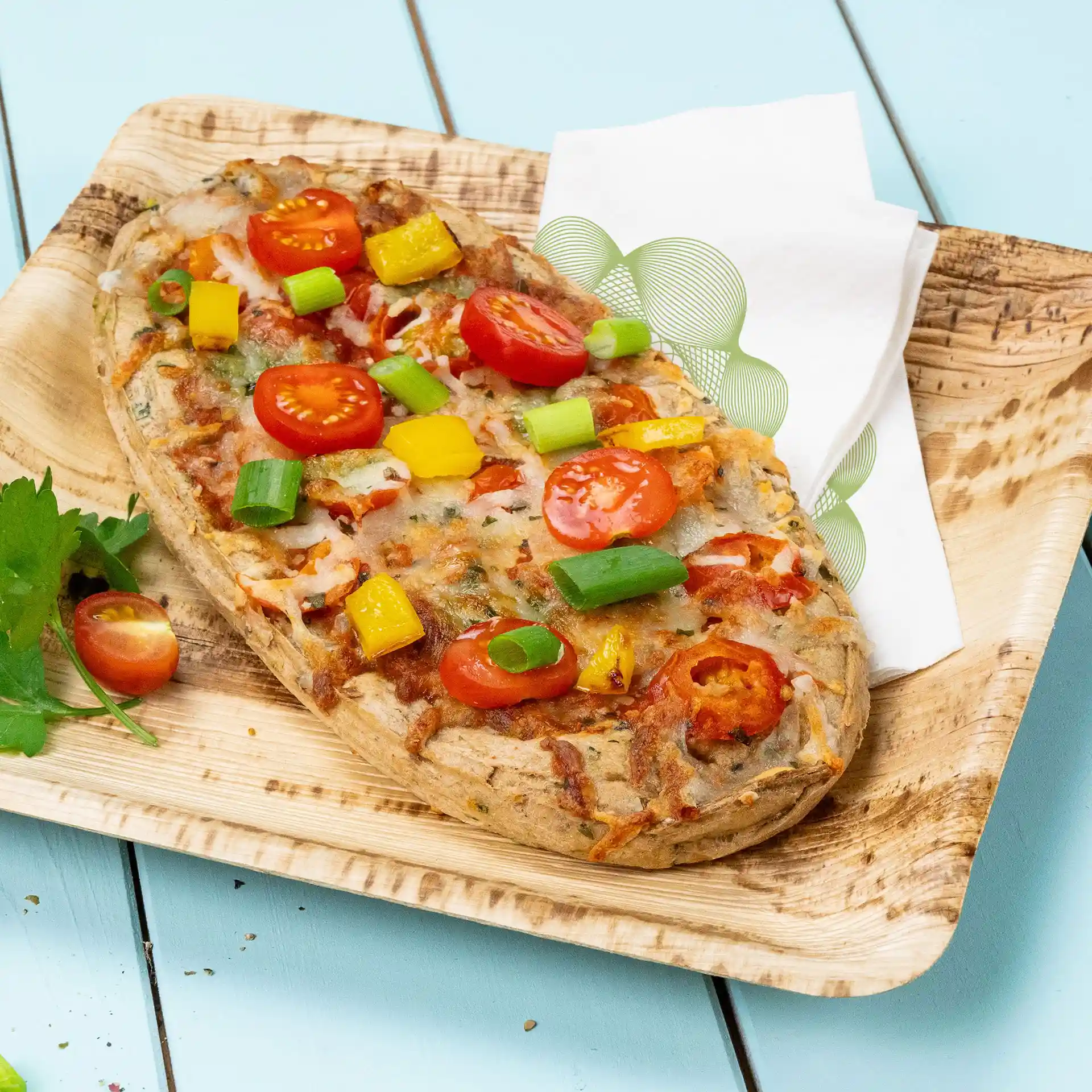 Pizza aux légumes garnie de tomates cerises, d'oignons verts et de poivrons jaunes sur une assiette en bois avec une serviette.