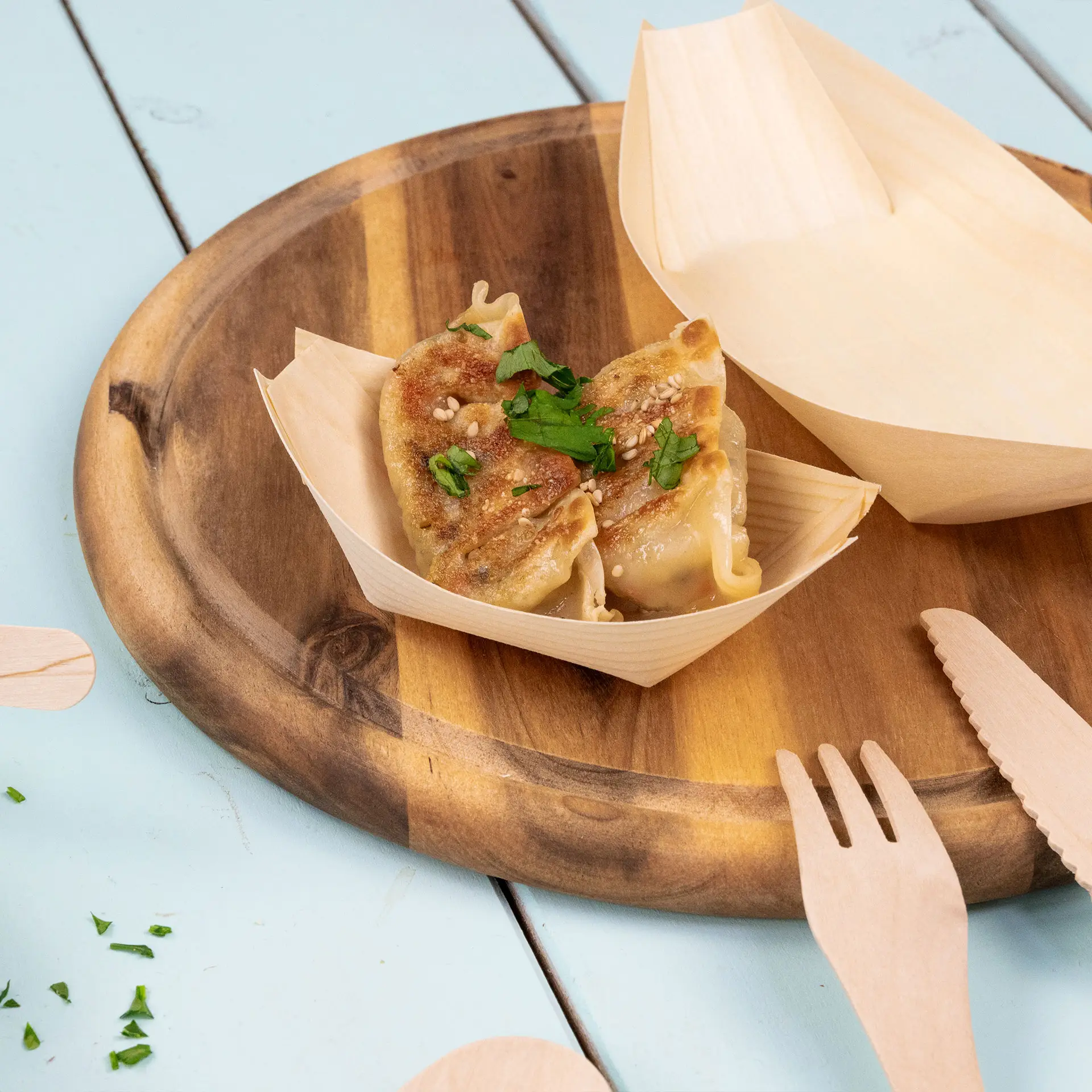 Holzboot-förmiger Behälter mit zwei mit Sesam und Petersilie garnierten Teigtaschen auf einem Holztablett.