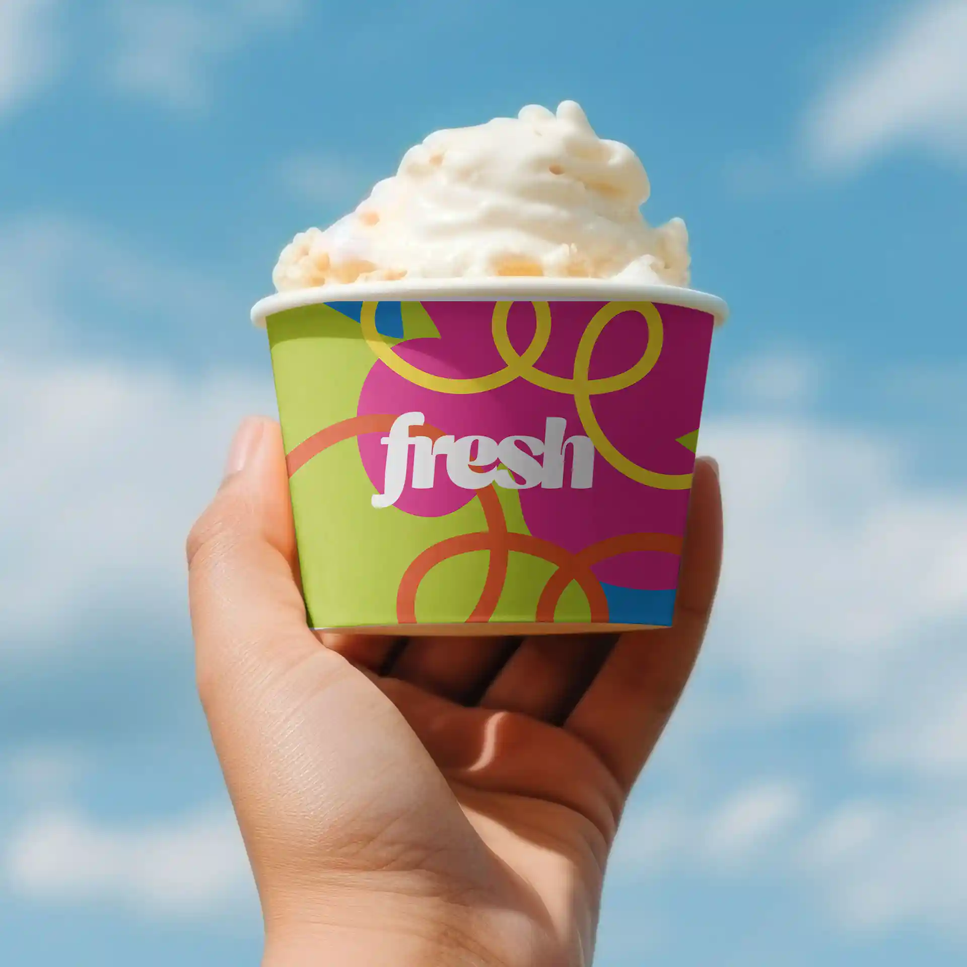 Runder Eisbecher in einer Hand, mit buntem Design und dem Wort "frisch" auf grünem Hintergrund.
