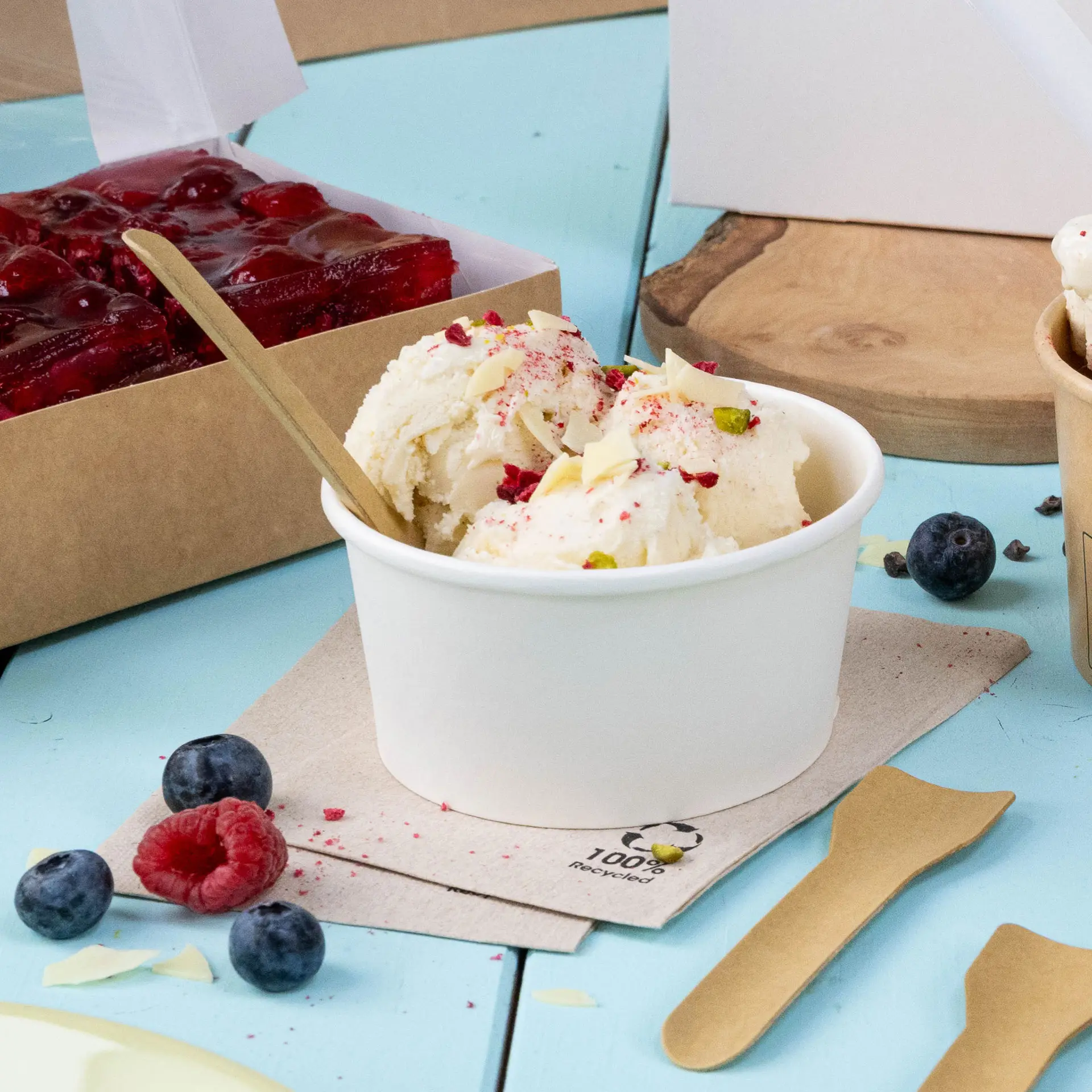 Eiscreme in einem weißen Becher, garniert mit Streuseln, umgeben von Himbeeren, Heidelbeeren und einer ungebleichten Serviette.