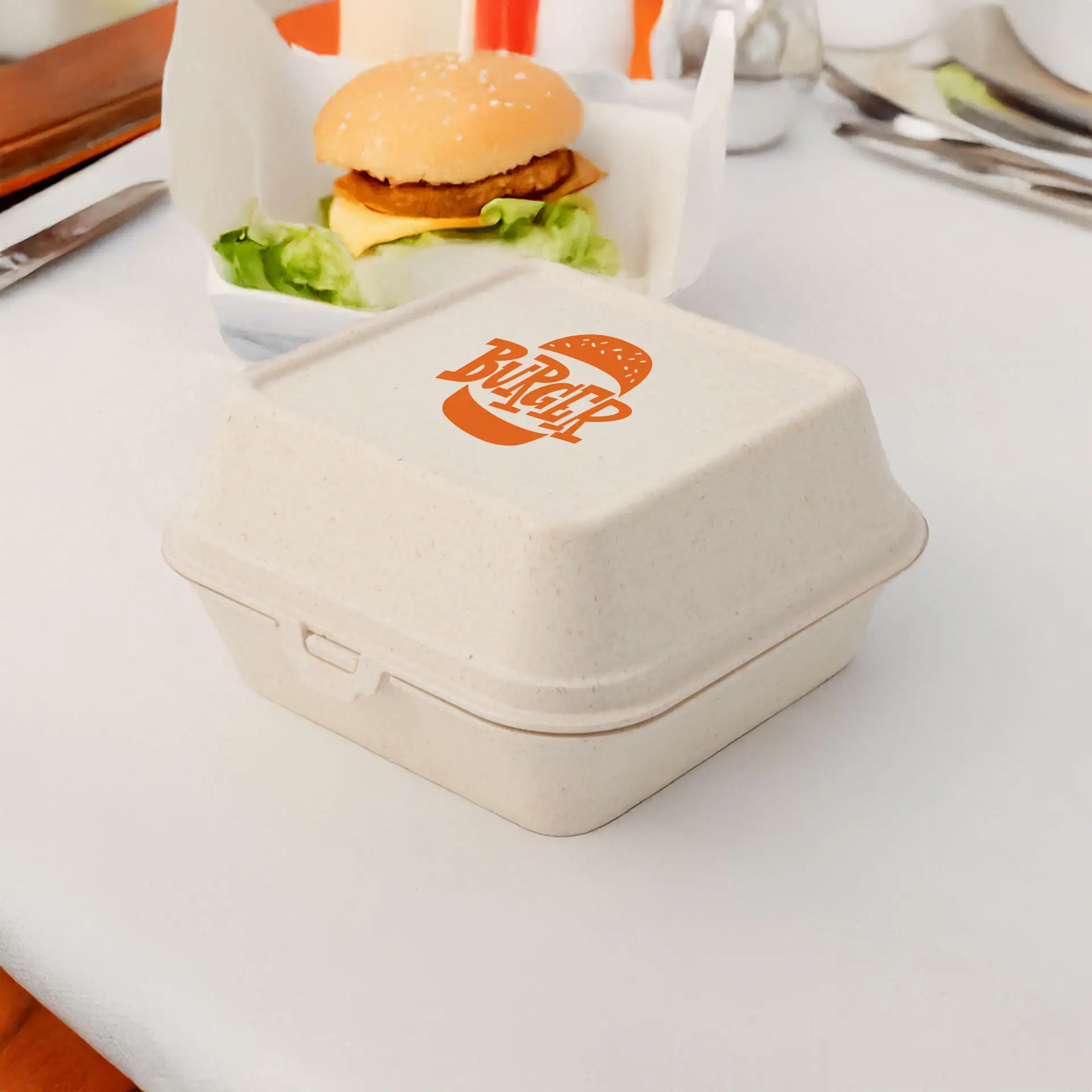 Cremeweiße wiederverwendbare Burgerbox mit gedrucktem Logo, geeignet für heiße und kalte Speisen, neben einem Burger auf einem Tisch.