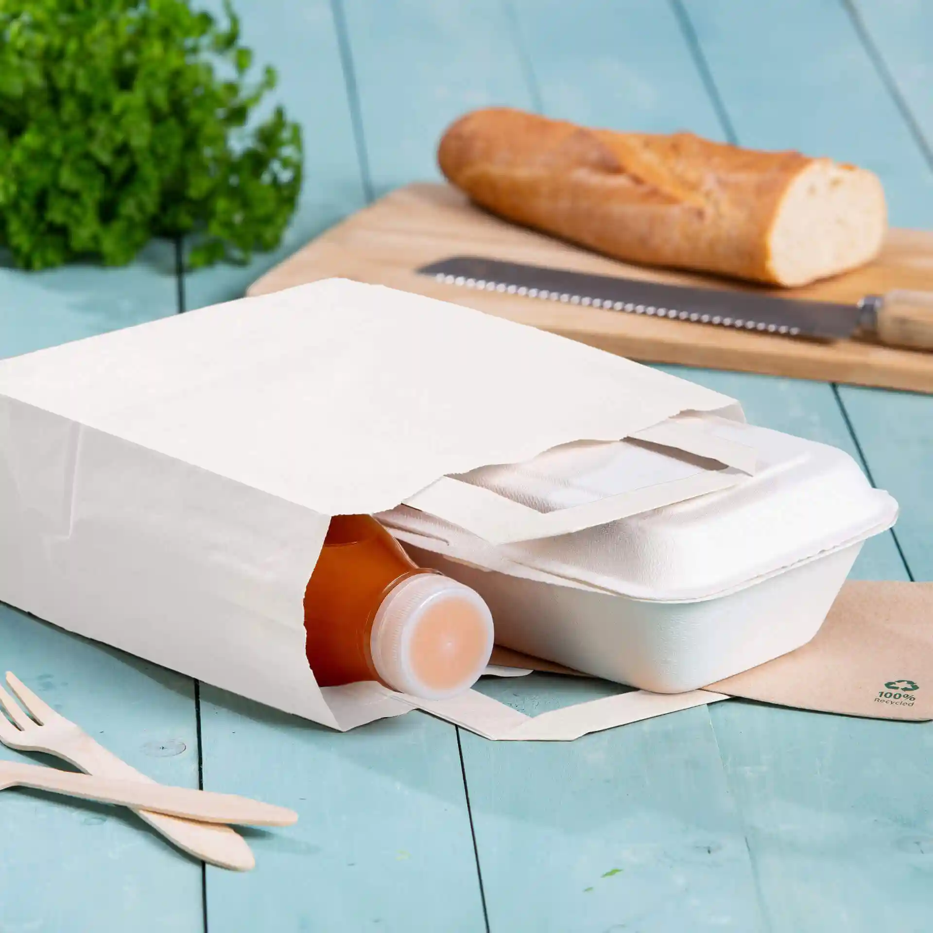 Weiße Kraftpapier-Tragetasche mit einer Flasche und einem Takeout-Behälter, auf einer blauen Holzoberfläche.