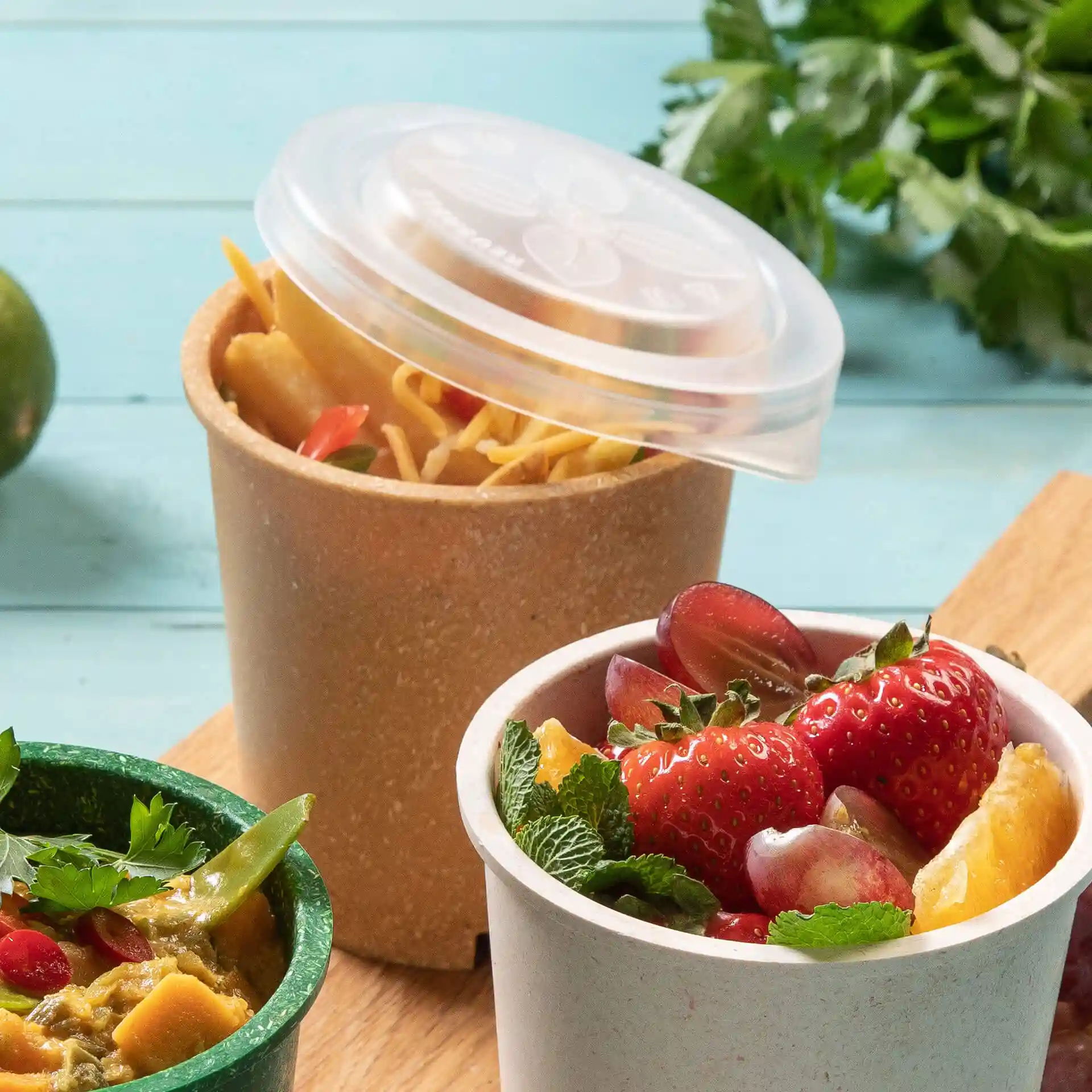 Immagine di due contenitori per alimenti: uno con noodles e un coperchio trasparente, l'altro con frutta, su una superficie di legno.