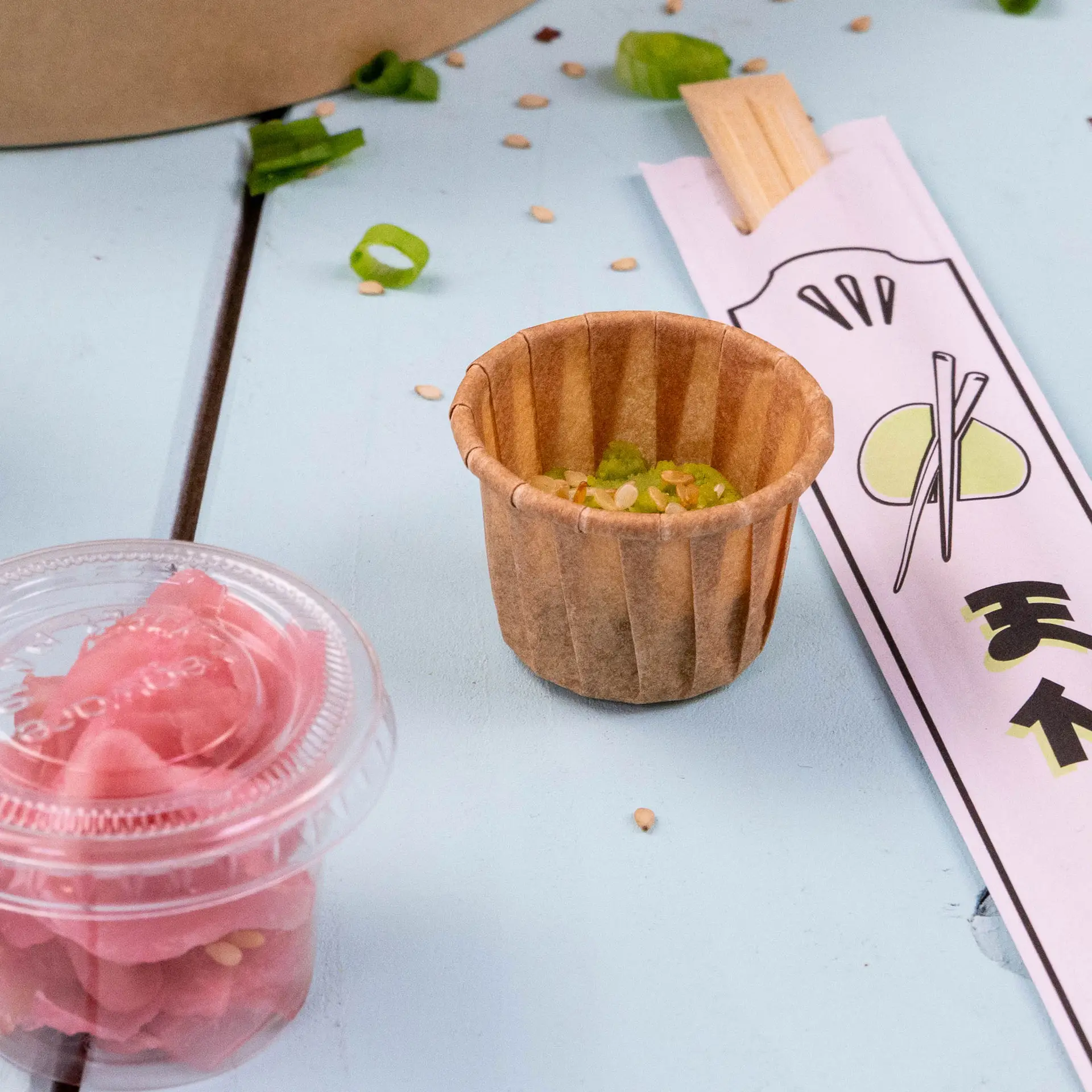 Gobelet en papier marron pour dips et sauces, capacité de 15 ml, avec graines de sésame et oignons verts hachés à côté du gingembre mariné et des baguettes.