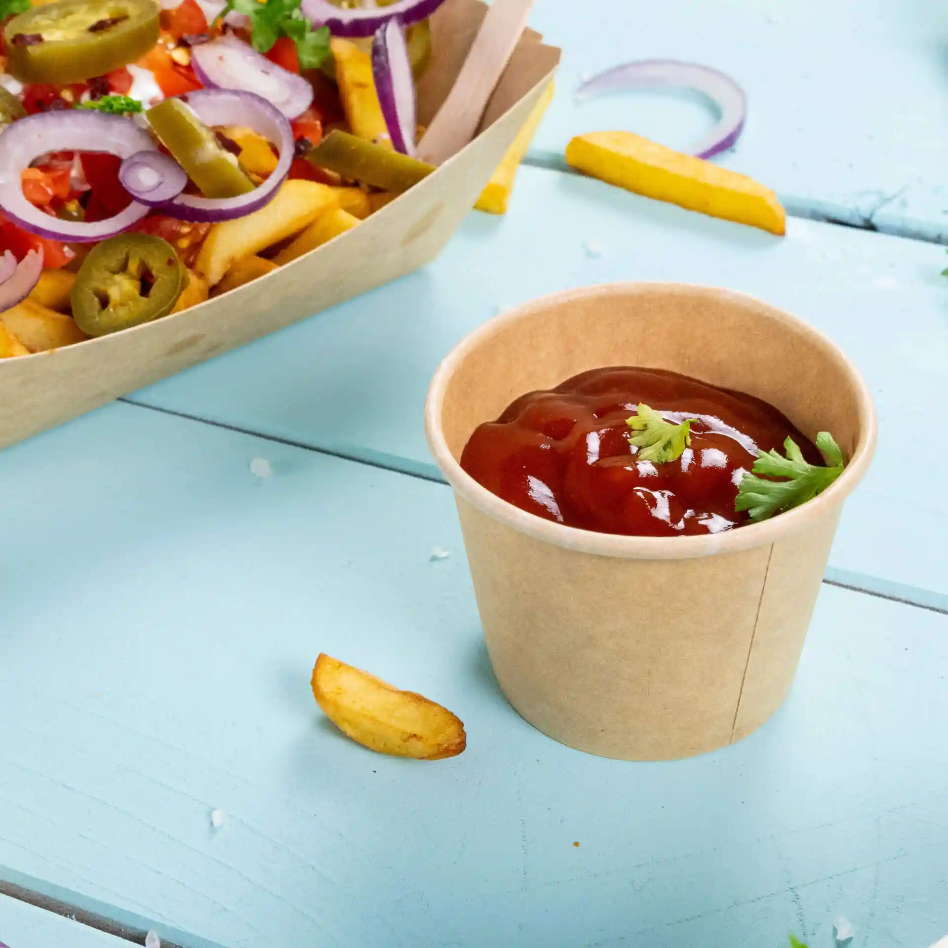 Contenitore rotondo marrone per deli con ketchup, guarnito con un piccolo pezzo di coriandolo, su una superficie in legno blu.