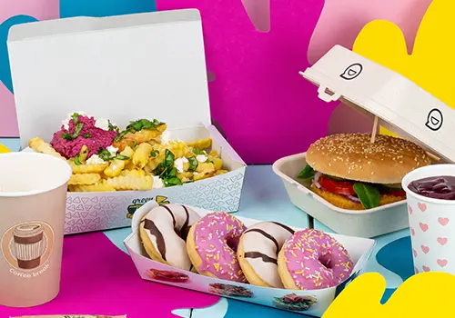 Karton mit einem Burger mit Käse, Zwiebeln, Salat und Saucen; dazu goldene Pommes und Zwiebelringe; zwei kleine Saucen enthalten.