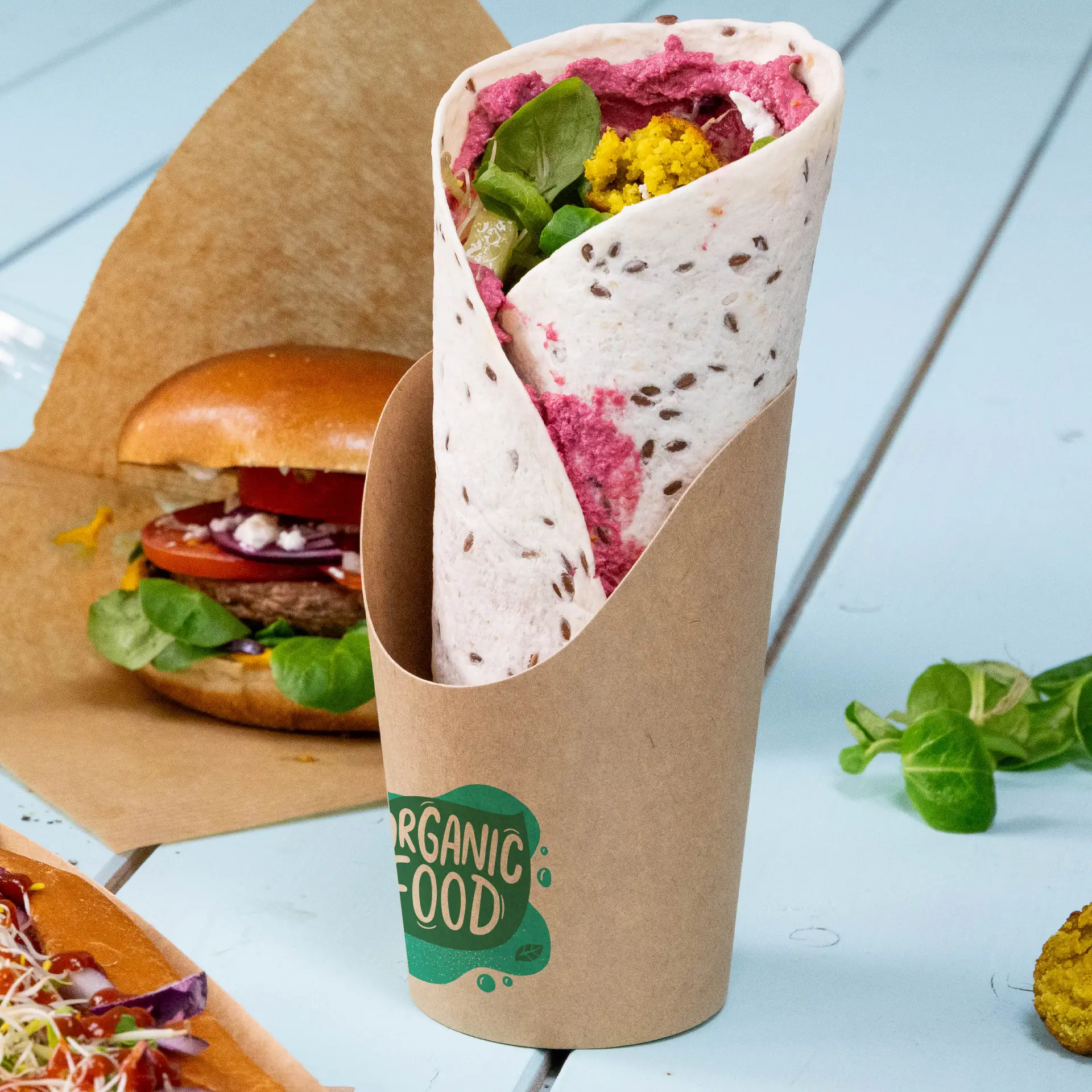 Gobelet en carton kraft personnalisé, rempli d'un wrap coloré. Arrière-plan avec un burger et des légumes frais.