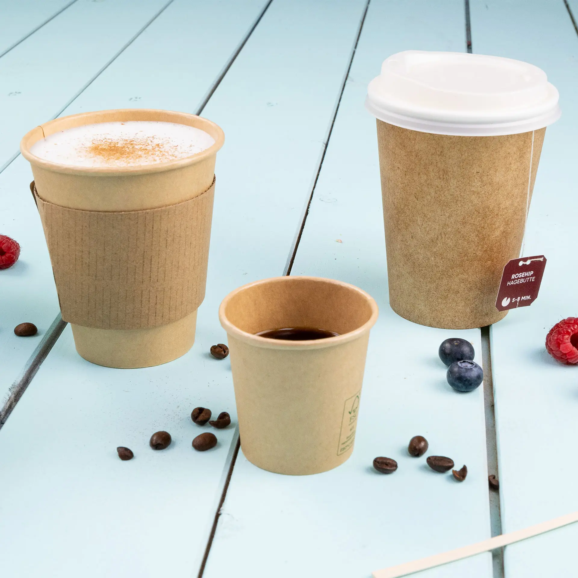 Bild von drei braunen Bechern auf einer blauen Holzoberfläche, darunter ein größerer Becher mit Sleeve, ein mittlerer Becher und ein kleiner Becher.