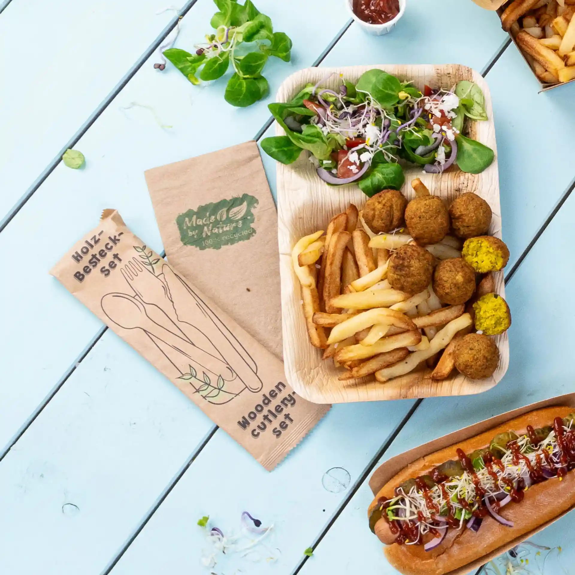 Immagine di un set di posate in legno con coltello, forchetta e cucchiaio, accanto a un piatto di patatine, falafel e insalata.