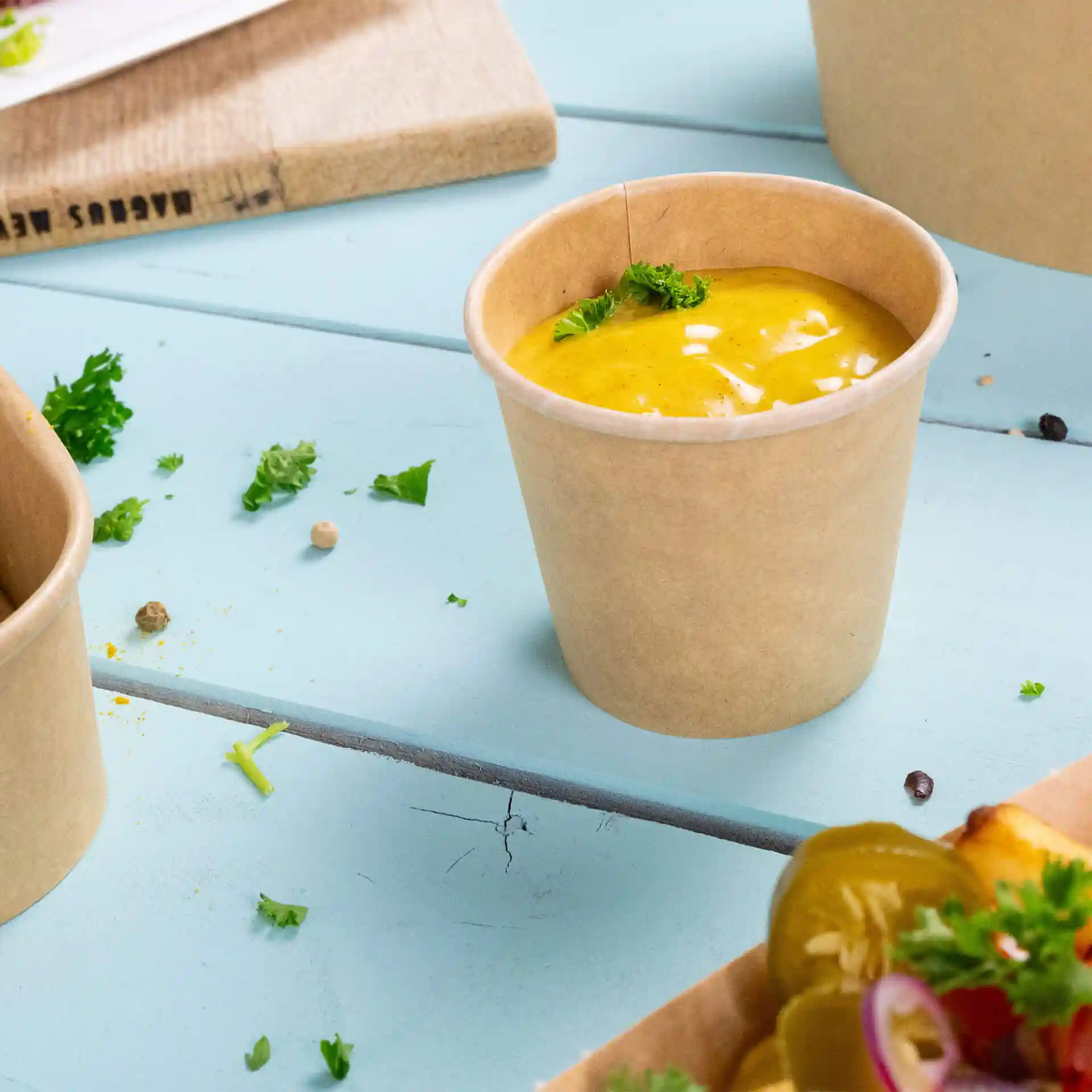 Cup in carta marrone con rivestimento ecologico, riempito di salsa e guarnito con un piccolo pezzo di prezzemolo.