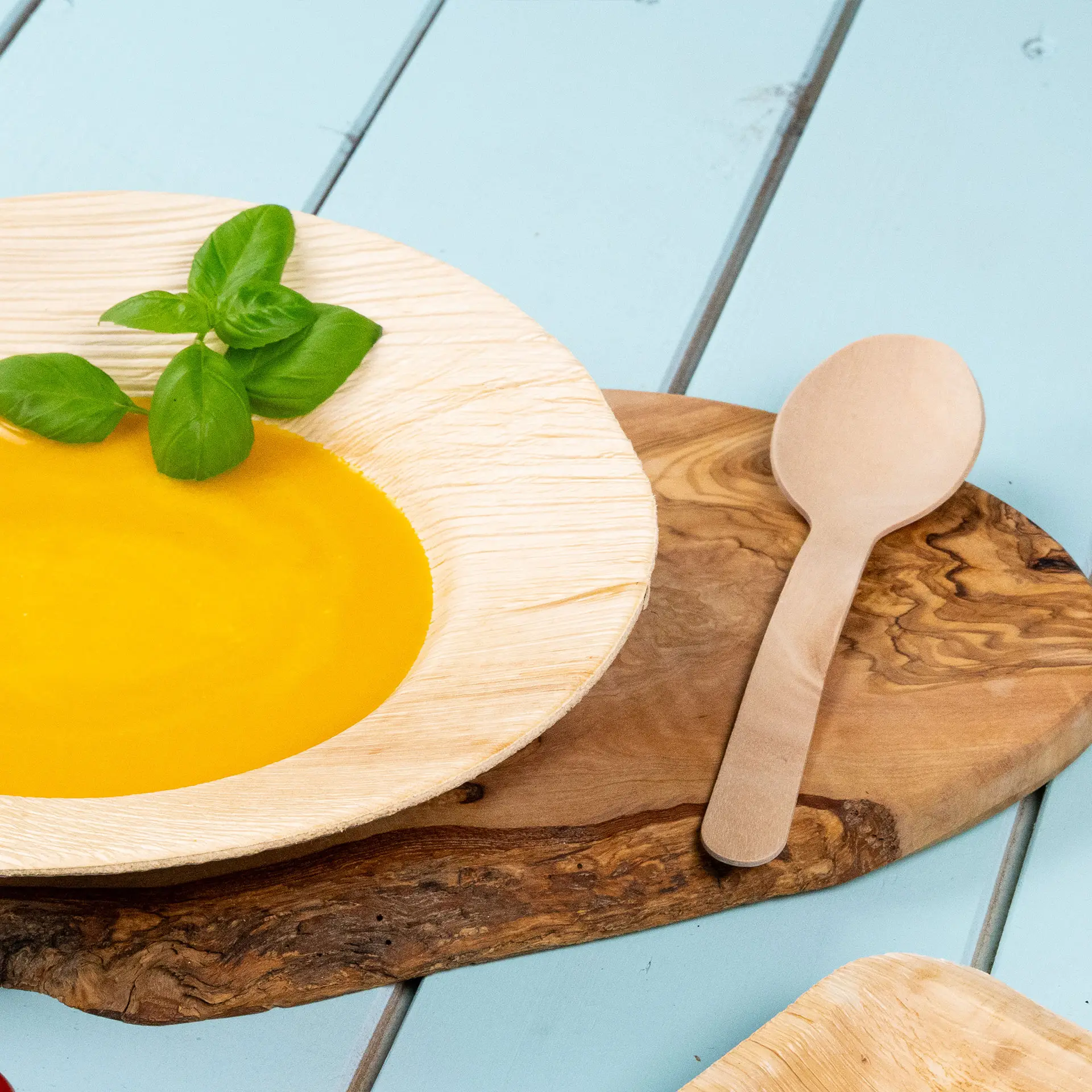 Schüssel mit gelber Suppe und einem Basilikumblatt, begleitet von einem Holzlöffel auf einem Holzbrett.