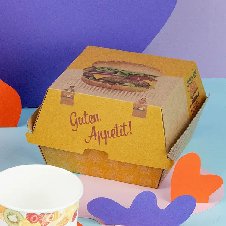 Boîtes à burger marron et blanches avec le texte "BURGER", un burger avec un pain au sésame et des frites sur une surface en bois.