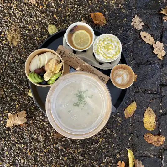 Plateau avec un bol de soupe clair, un bol de fruits mélangés et deux tasses de boissons, entouré de feuilles d'automne.