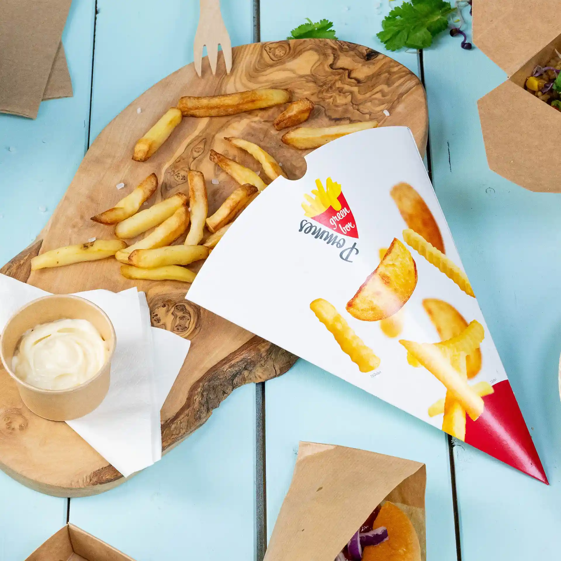 Cornet de frites imprimé avec des frites, un verre de sauce et une planche en bois sur une surface bleue.