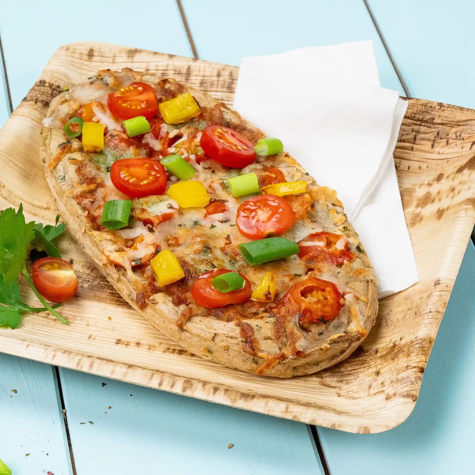 Focaccia con pomodorini, peperoni gialli e cipollotti su un piatto di legno con un tovagliolo.