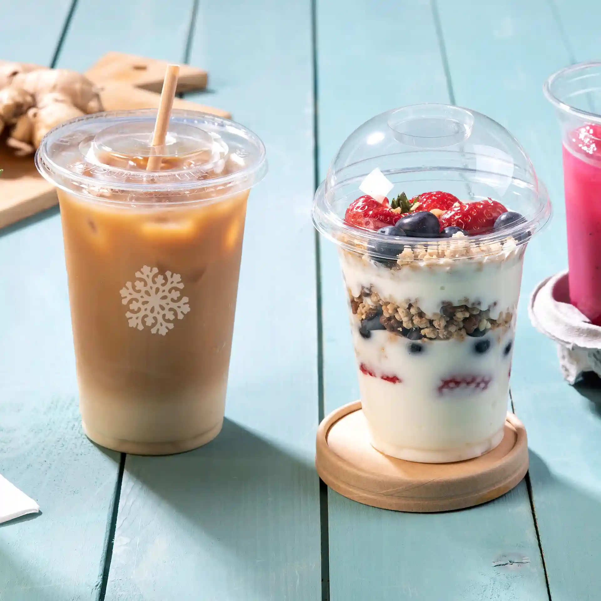 Bicchiere PLA trasparente da 12 oz con caffè freddo e un parfait con granola e frutti di bosco su una superficie di legno.