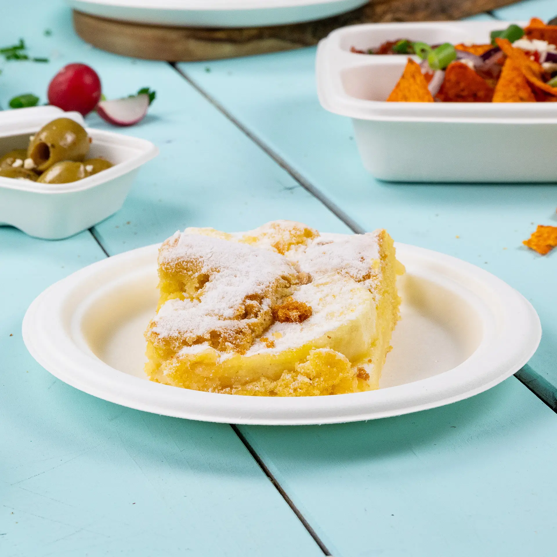 Stück Kuchen auf einem runden, biologisch abbaubaren Zuckerrohr-Teller, auf einem blauen Holztisch platziert.