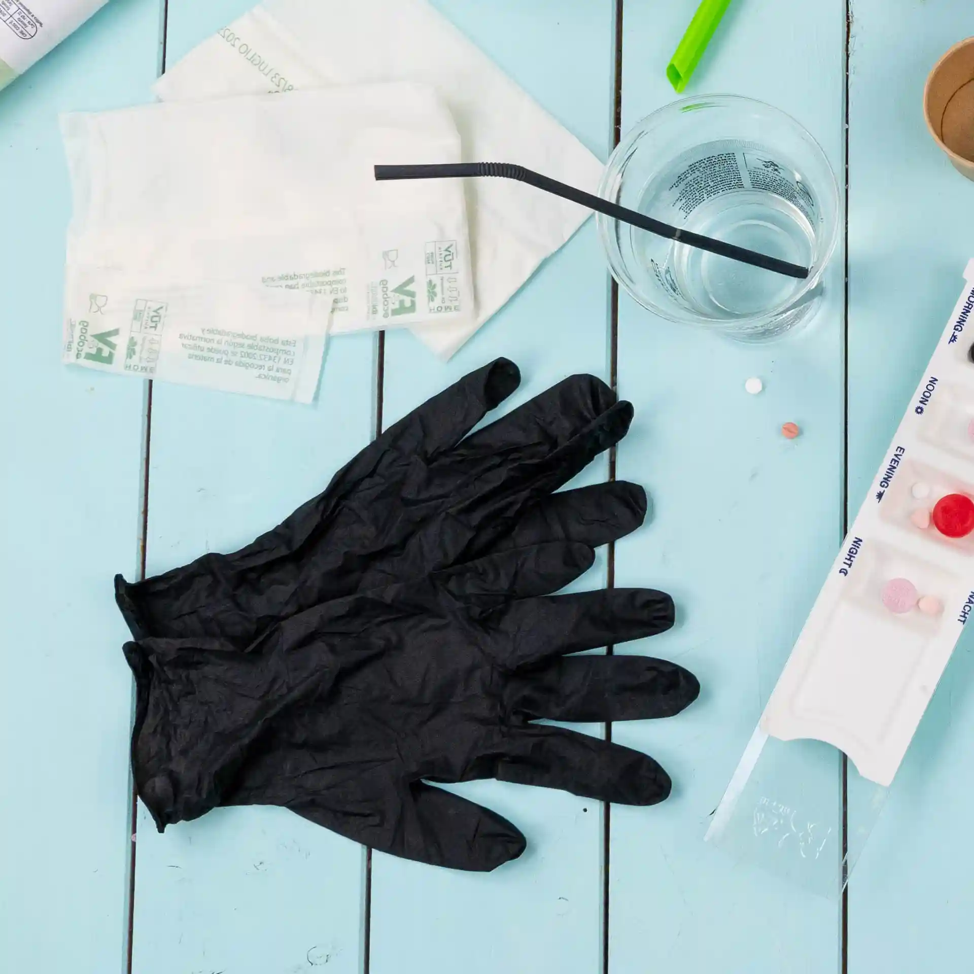 Gants en nitrile noirs posés sur une surface bleue, avec un verre d'eau, une paille et divers objets à proximité.