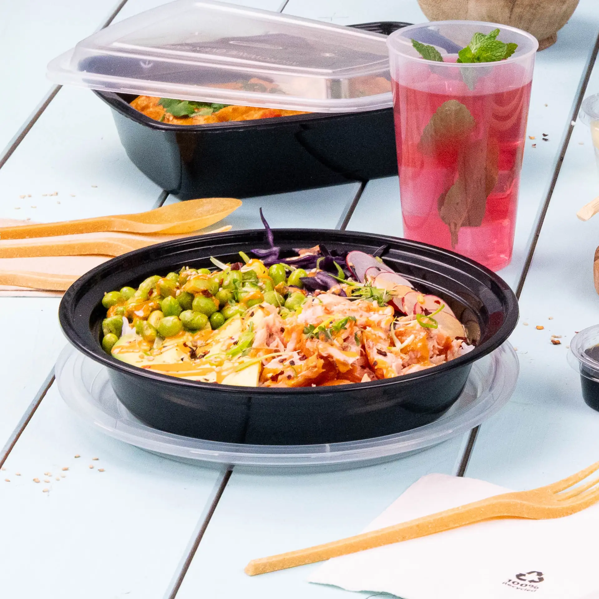 Wiederverwendbarer schwarzer Teller für warme und kalte Gerichte, serviert mit Erbsen, geriebenem Gemüse und einem Getränk; mit Holzutensilien.