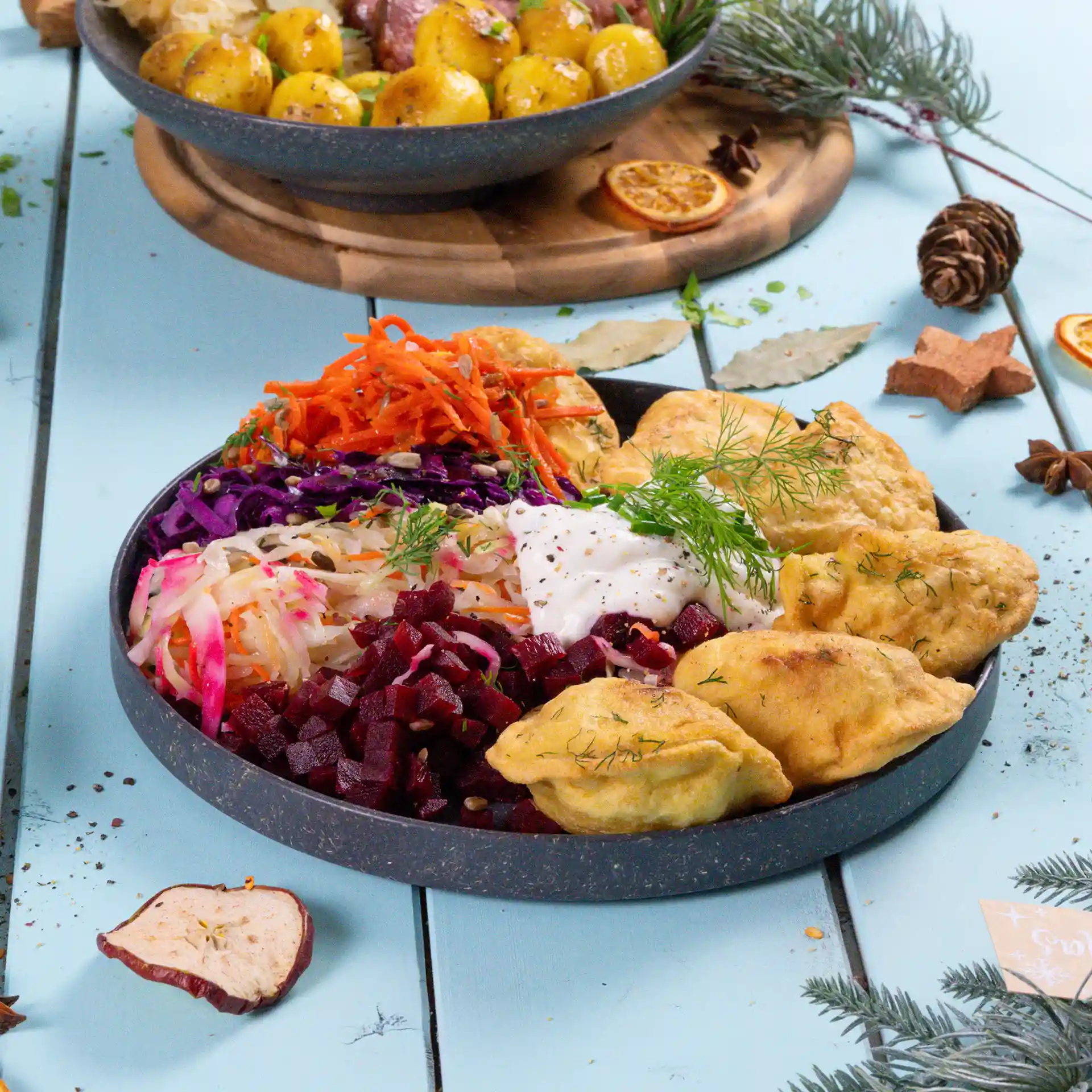 Runde graue wiederverwendbare Platte, gefüllt mit verschiedenen bunten Salaten, Dips und frittierten Speisen, auf einer blauen Oberfläche.
