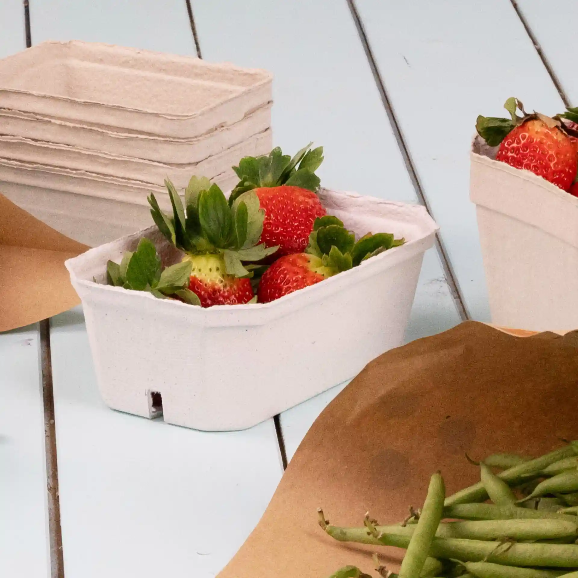 Conteneur contenant des fraises, en pulpe de bois blanc, avec d'autres conteneurs vides en arrière-plan.