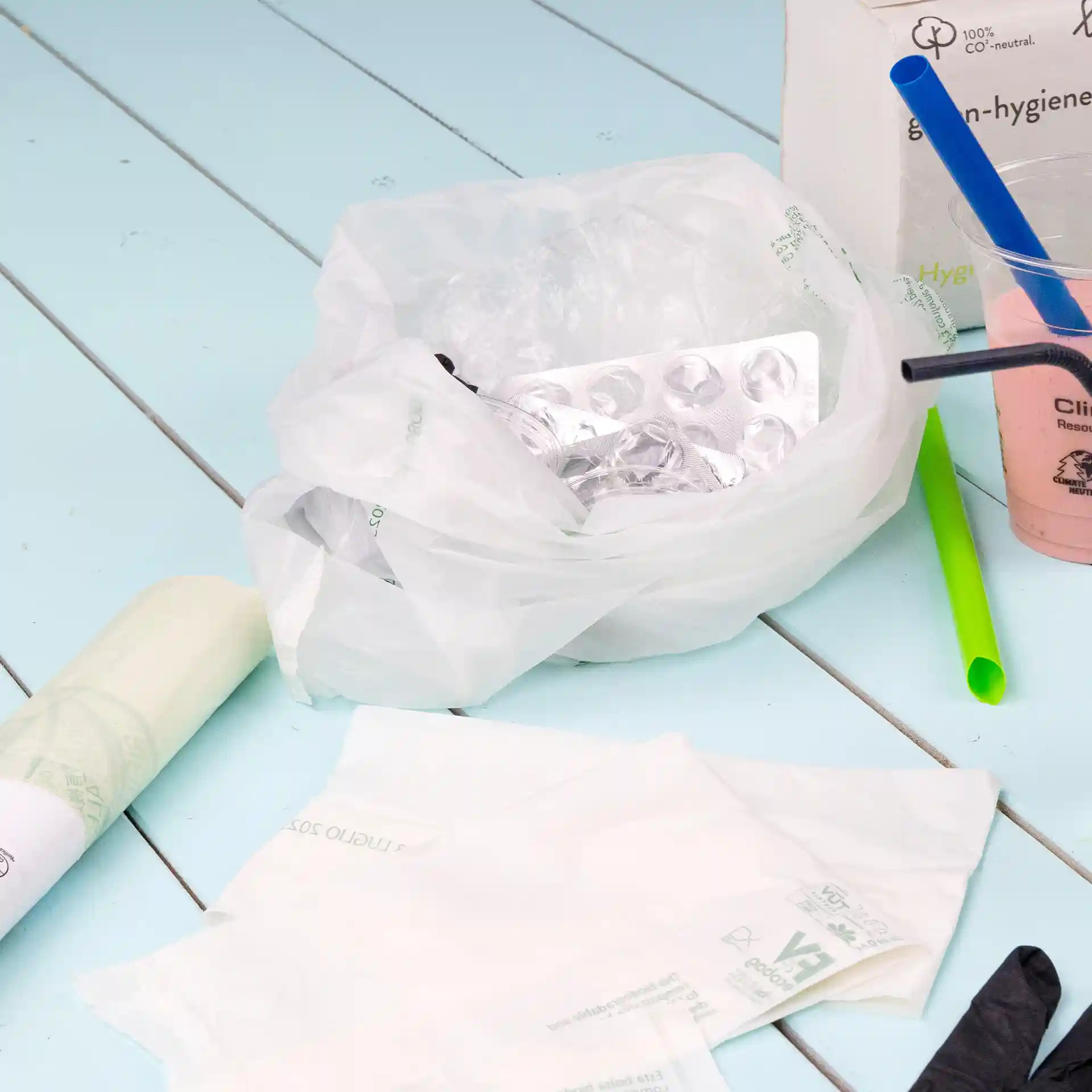 Sacchetto bio trasparente con contenuto accartocciato, inclusa una confezione blister, su una superficie blu chiaro.