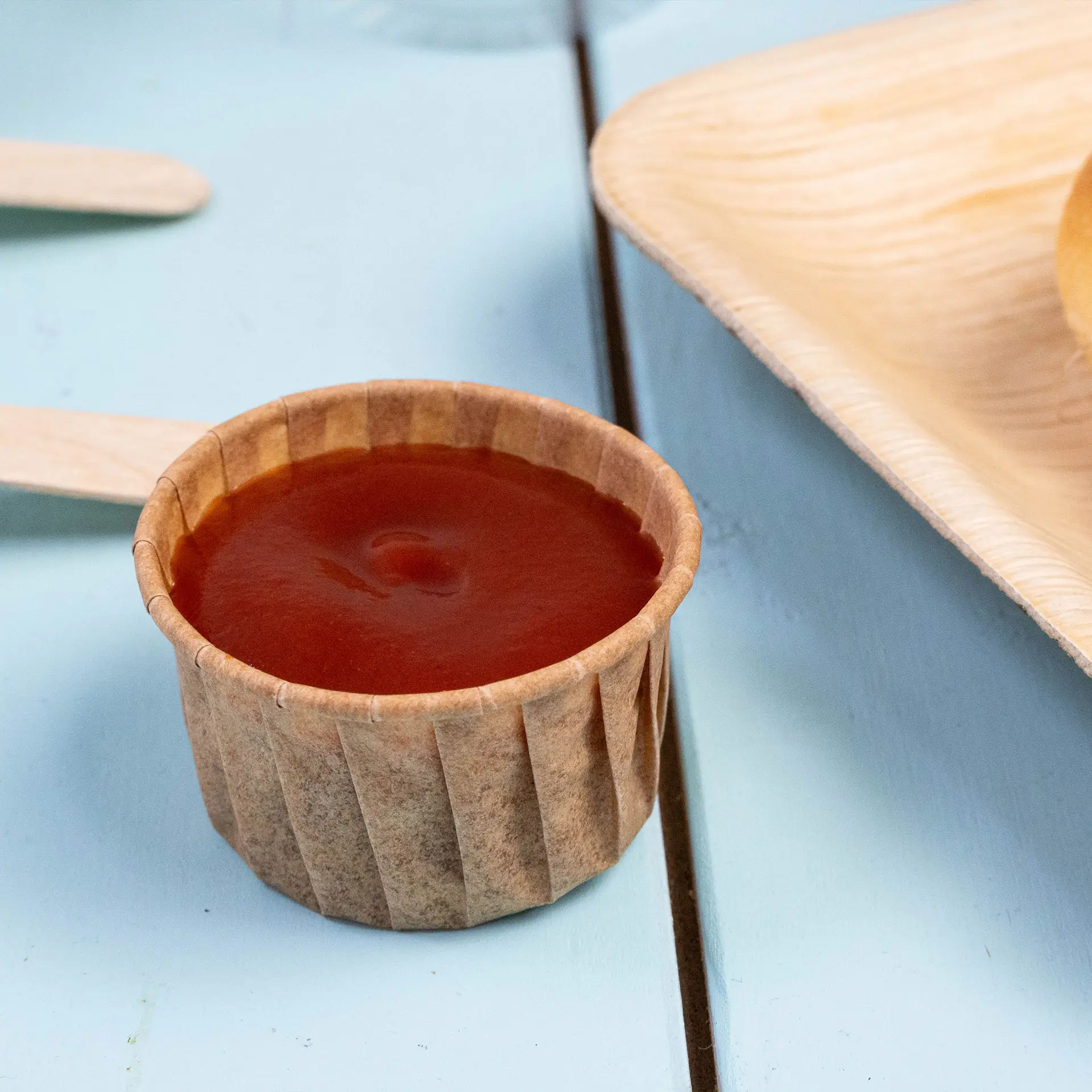 Gobelet en papier brun rempli de sauce, adapté pour les trempettes et les petites portions, sur une surface de table bleue.